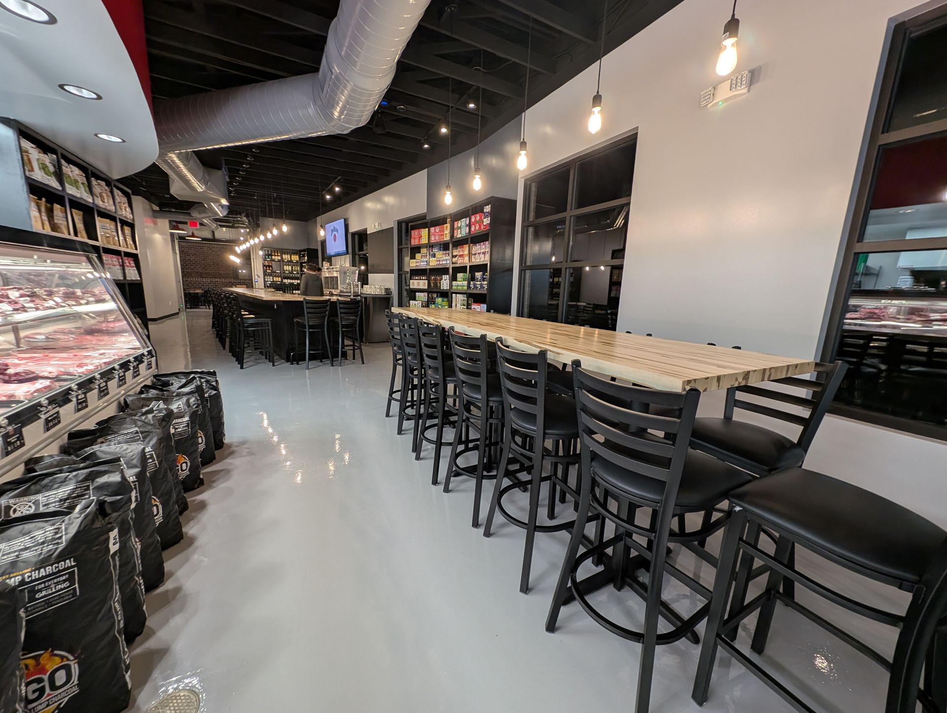 Modern bar interior with long counter, high stools, shelves of bottles, and glossy floor