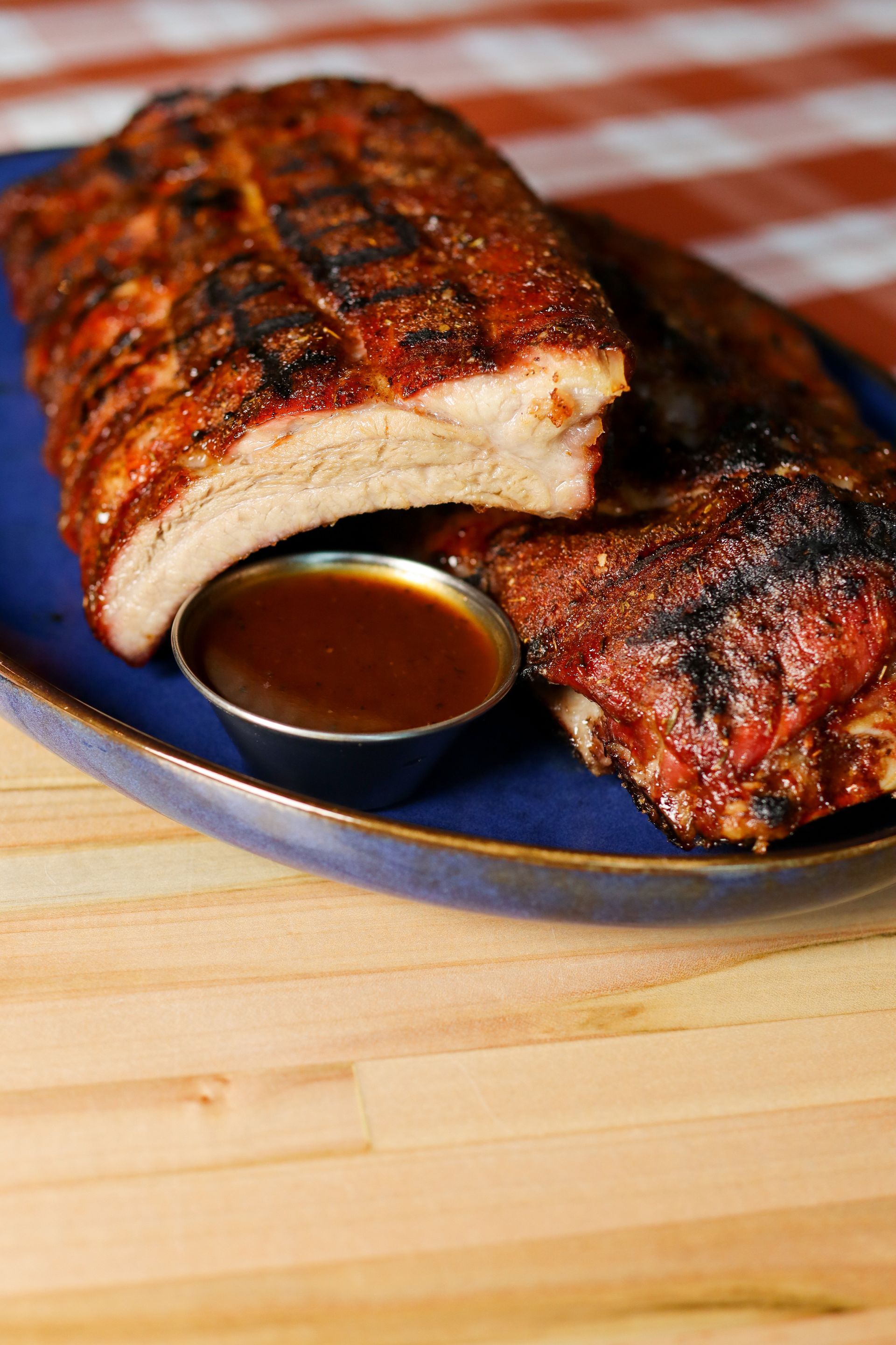 Barbecued ribs on a blue plate with dipping sauce on a wooden table