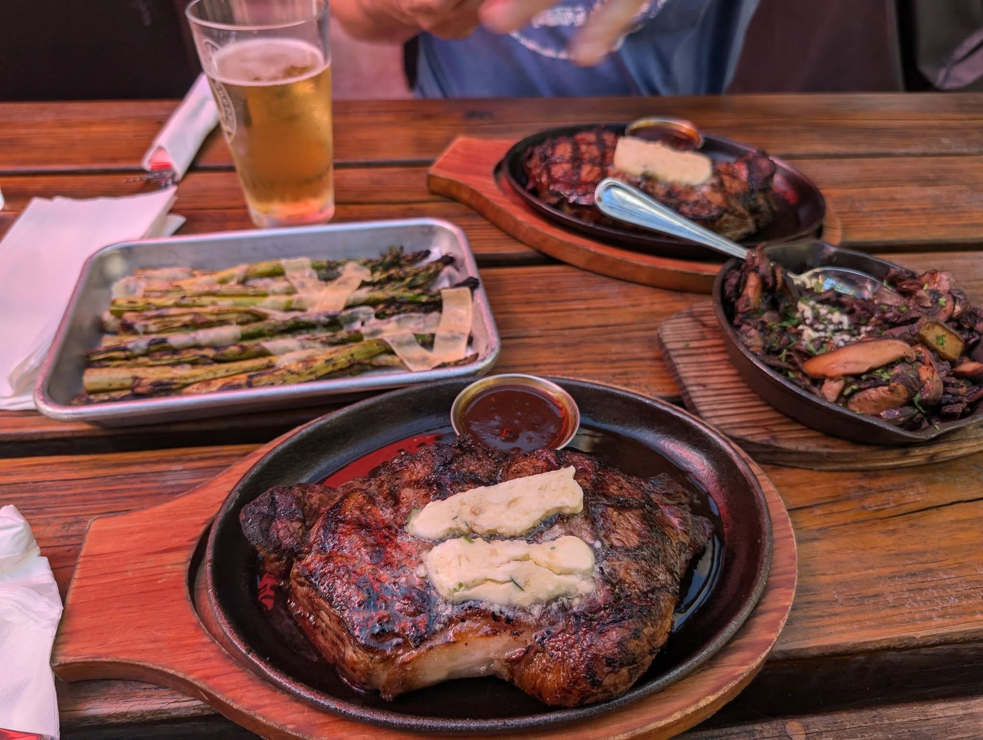 Three plates of grilled food on a wooden table with a beer glass