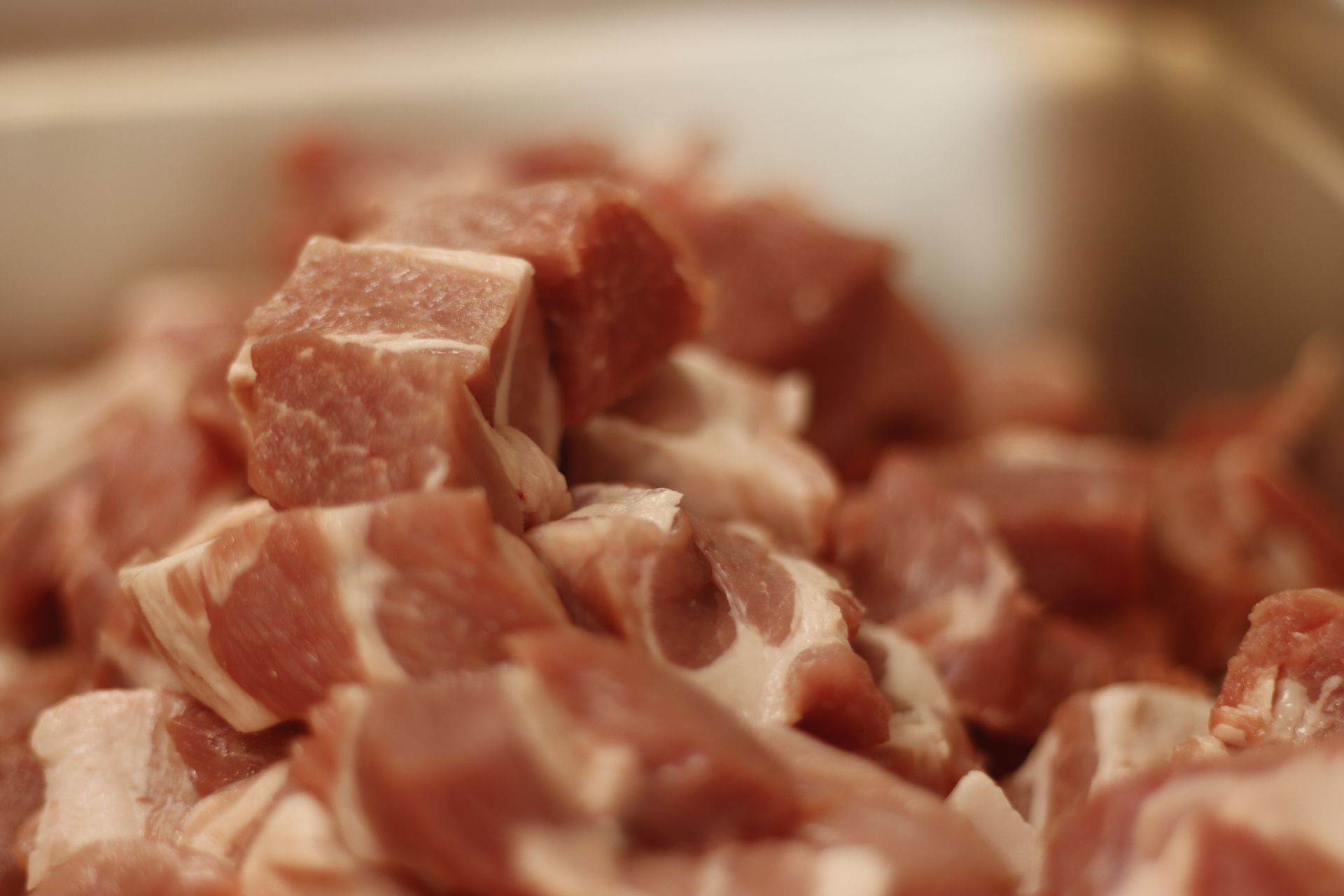 Close-up of diced raw pork with marbled fat, piled in a container.