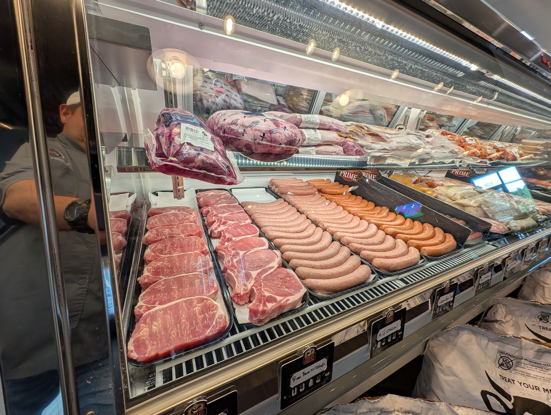 Butcher shop meat display in glass case with sausages, cuts of beef, and packaged items