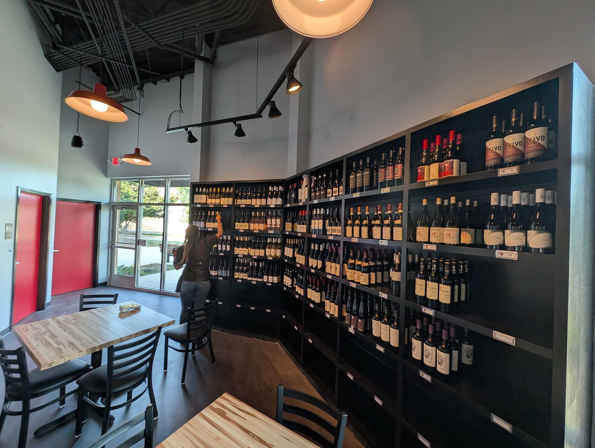 Modern wine shop interior with wall-to-wall shelves of bottled wine and a table with chairs near the window