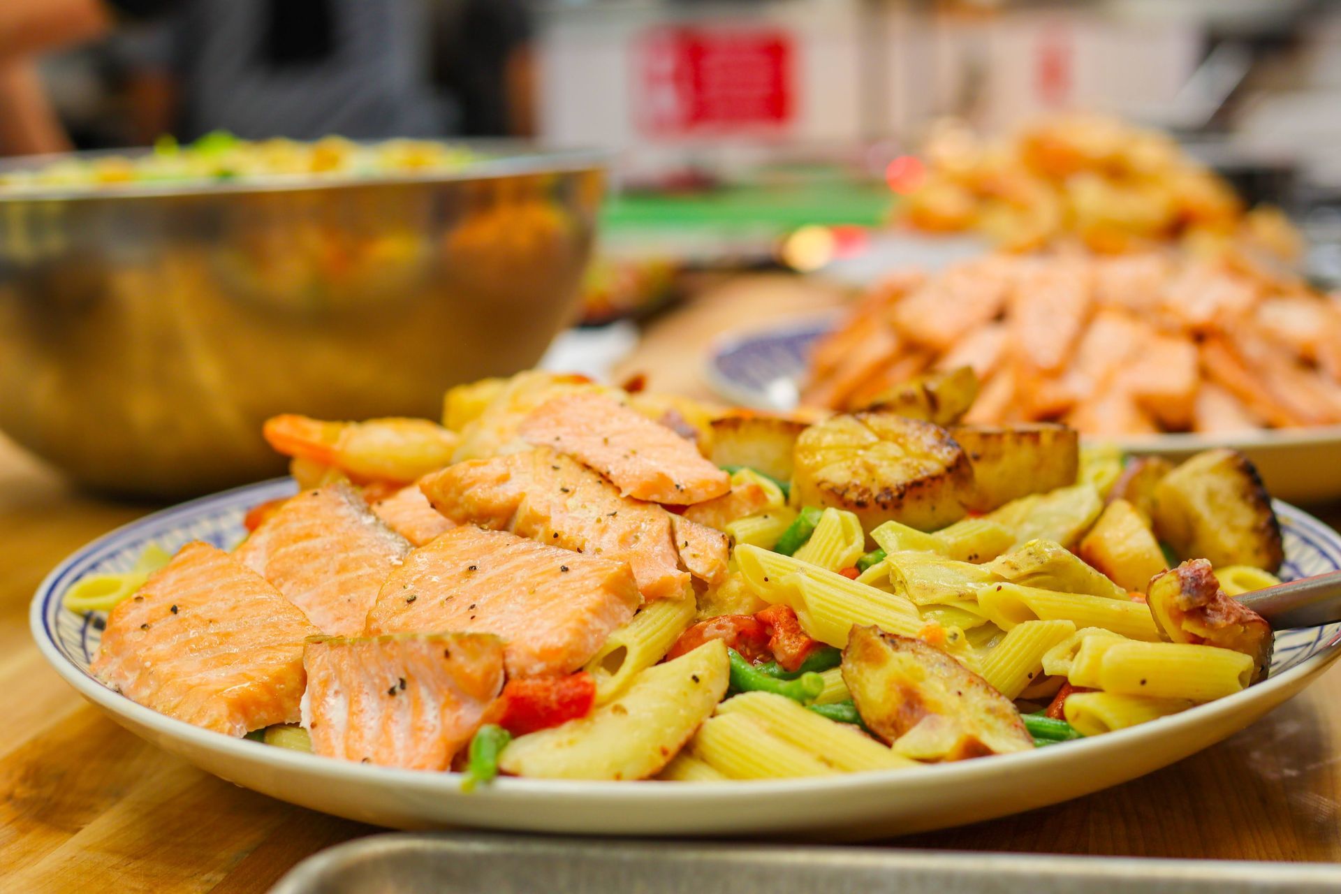 Plate of grilled salmon and vegetables on a table, with a blurred bowl and food in the background
