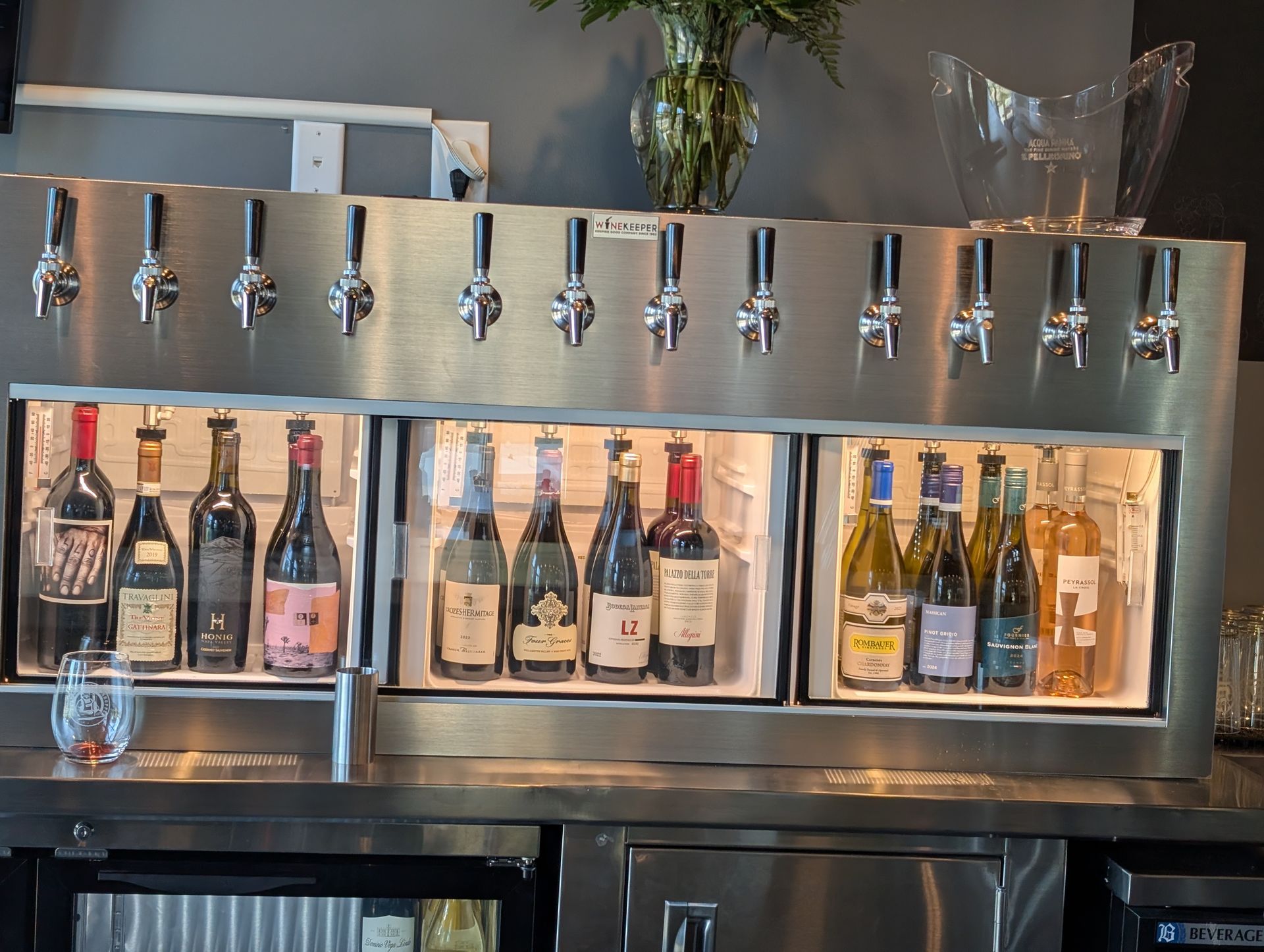 Stainless steel bar with beer taps above bottles of wine and liquor in a backlit display