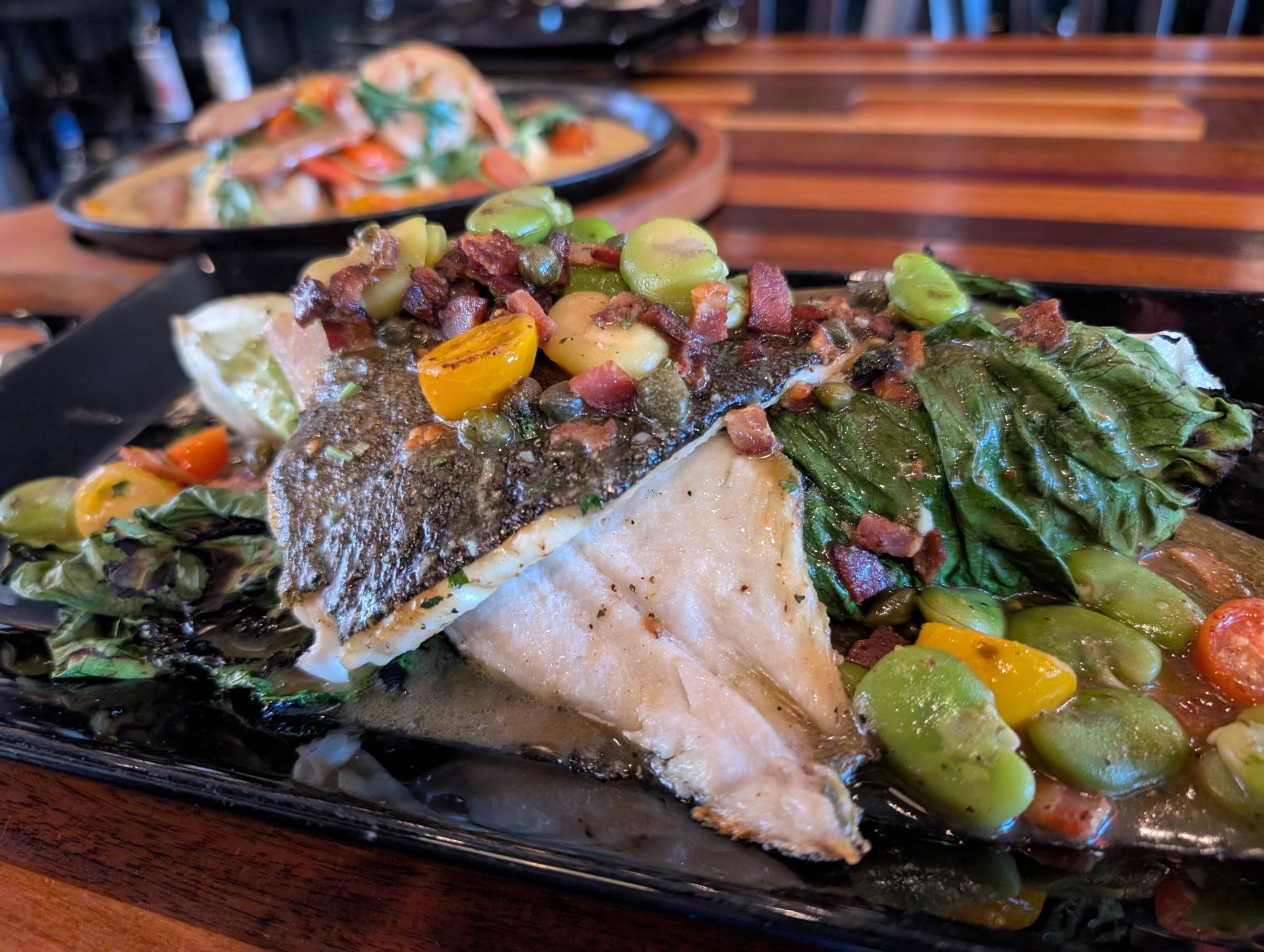 Seared fish fillet topped with salsa and vegetables on a black plate in a restaurant