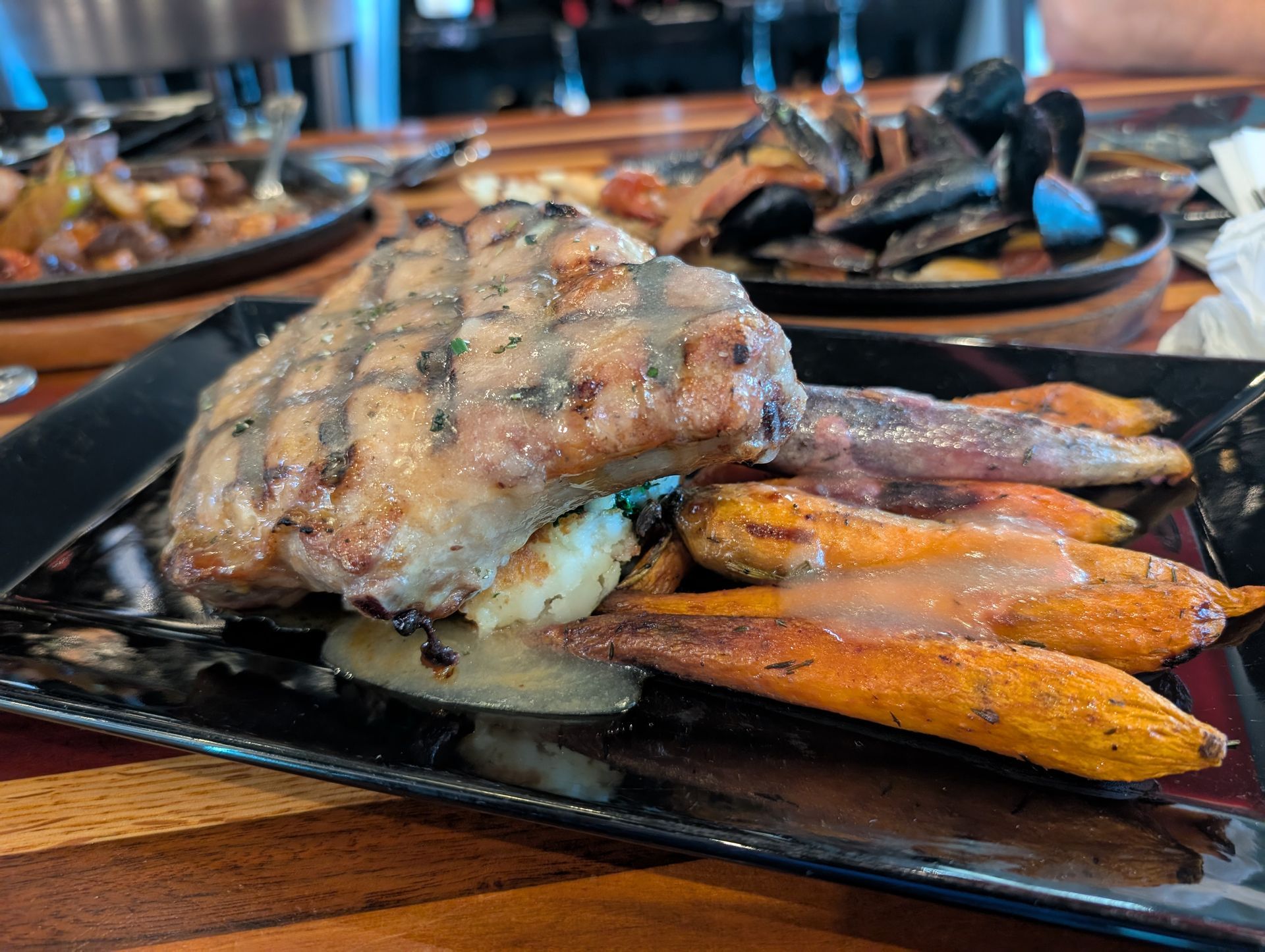 Grilled fish with roasted carrots and potatoes on a black plate in a restaurant setting