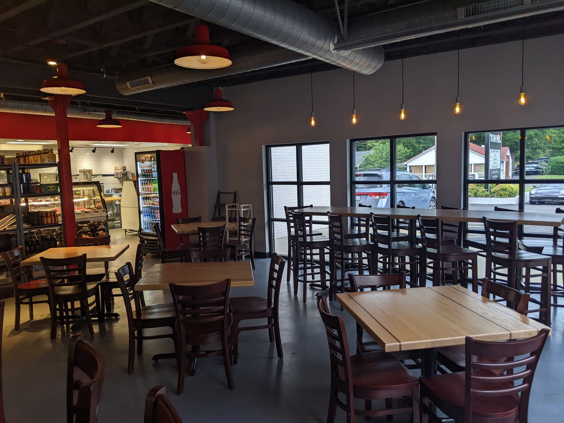 Empty restaurant dining room with tables and chairs, pendant lights, and large windows