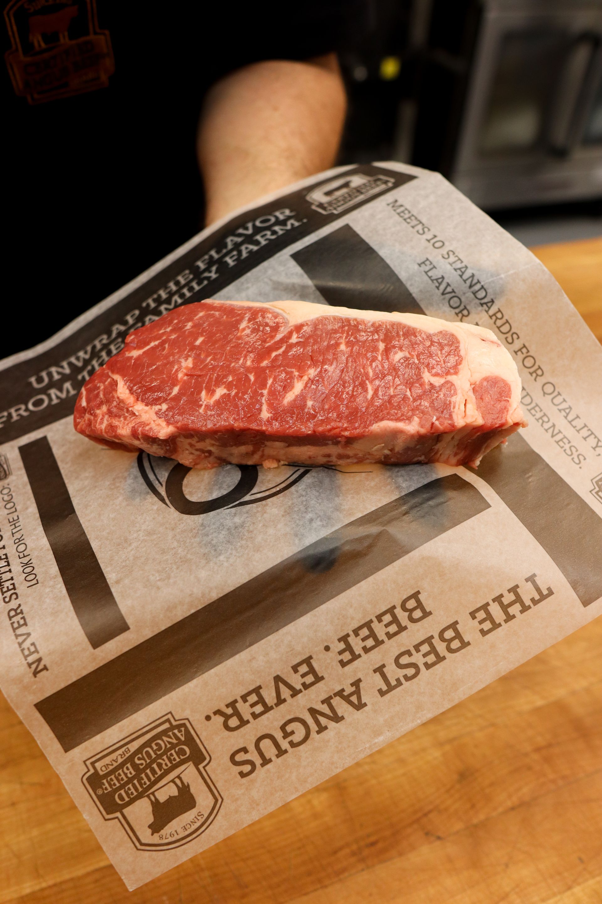 Raw marbled steak on butcher paper atop a wooden cutting board, ready to cook