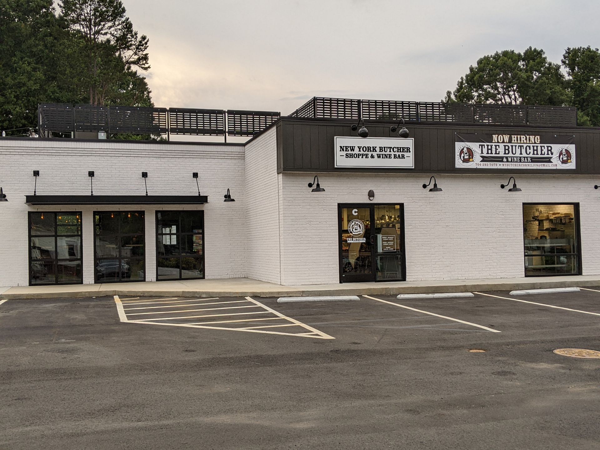 White storefront in a parking lot with glass doors, windows, and rooftop signage under a cloudy sky