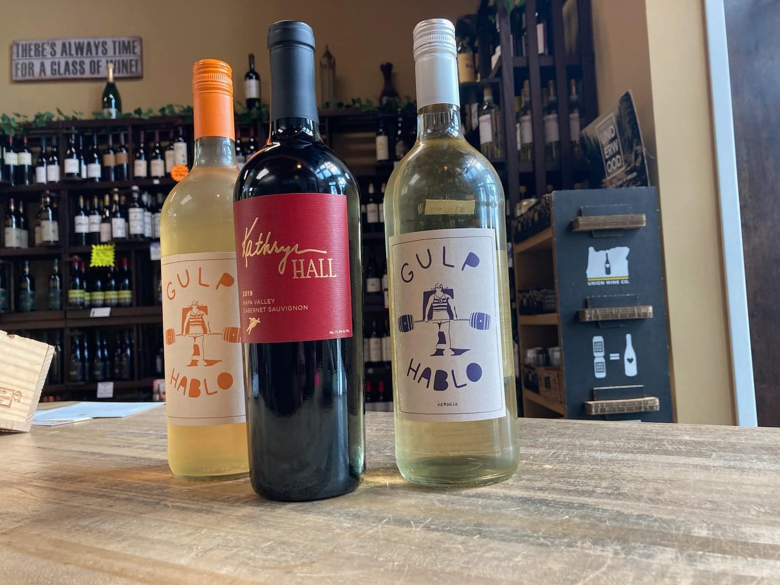 Three wine bottles on a counter: orange, red and white wine, in a shop.
