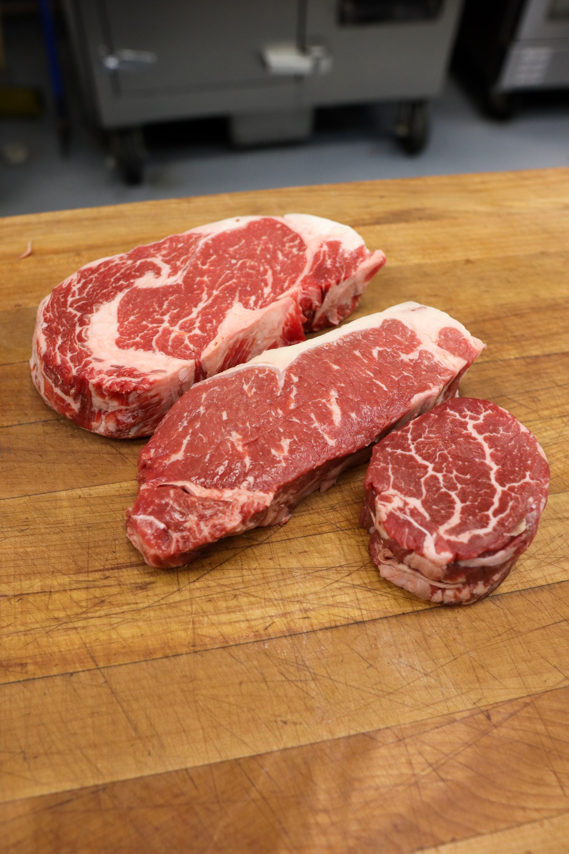 Three raw marbled steaks on a wooden cutting board in a kitchen setting