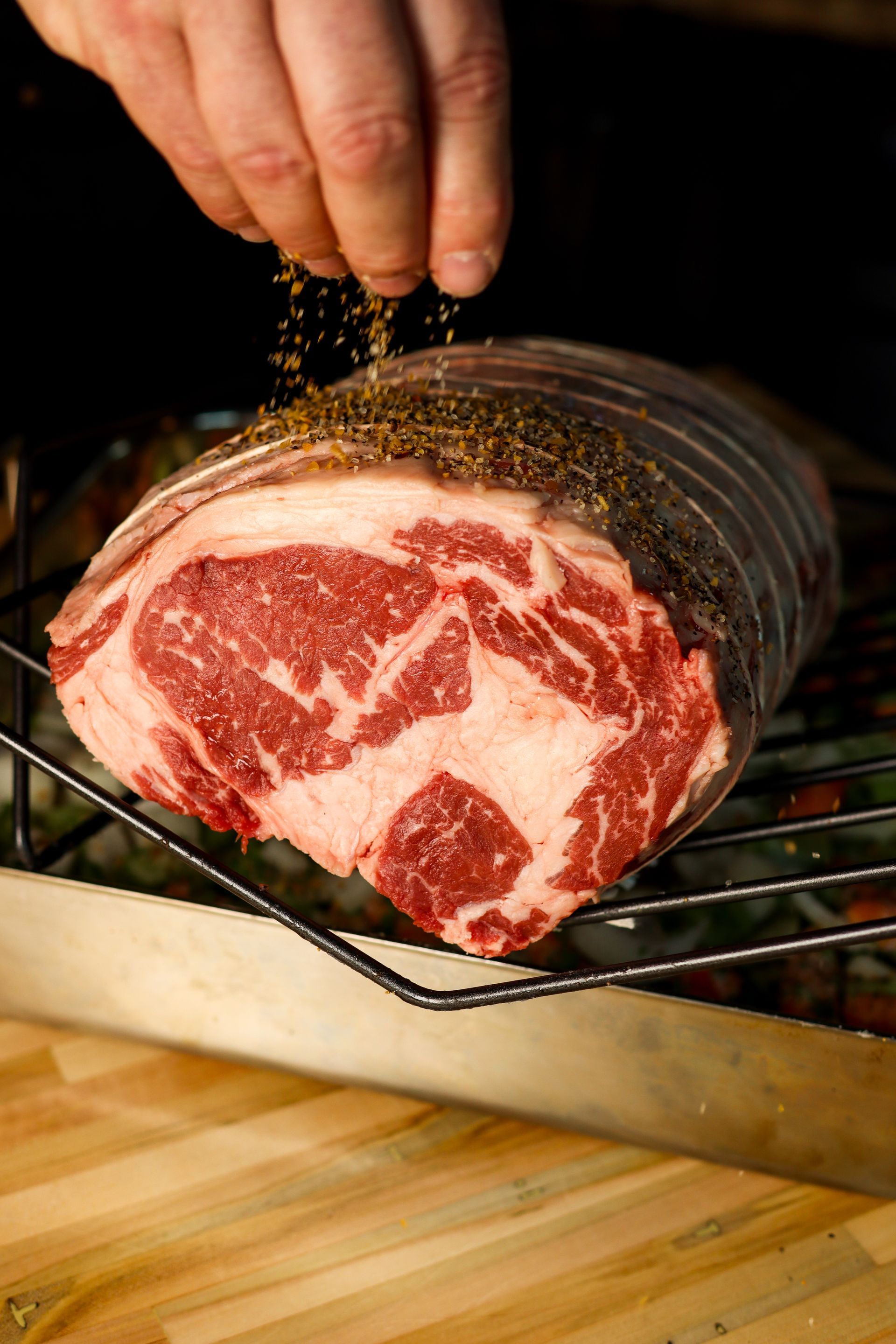 Seasoning marbled steak on a rack over a wooden surface