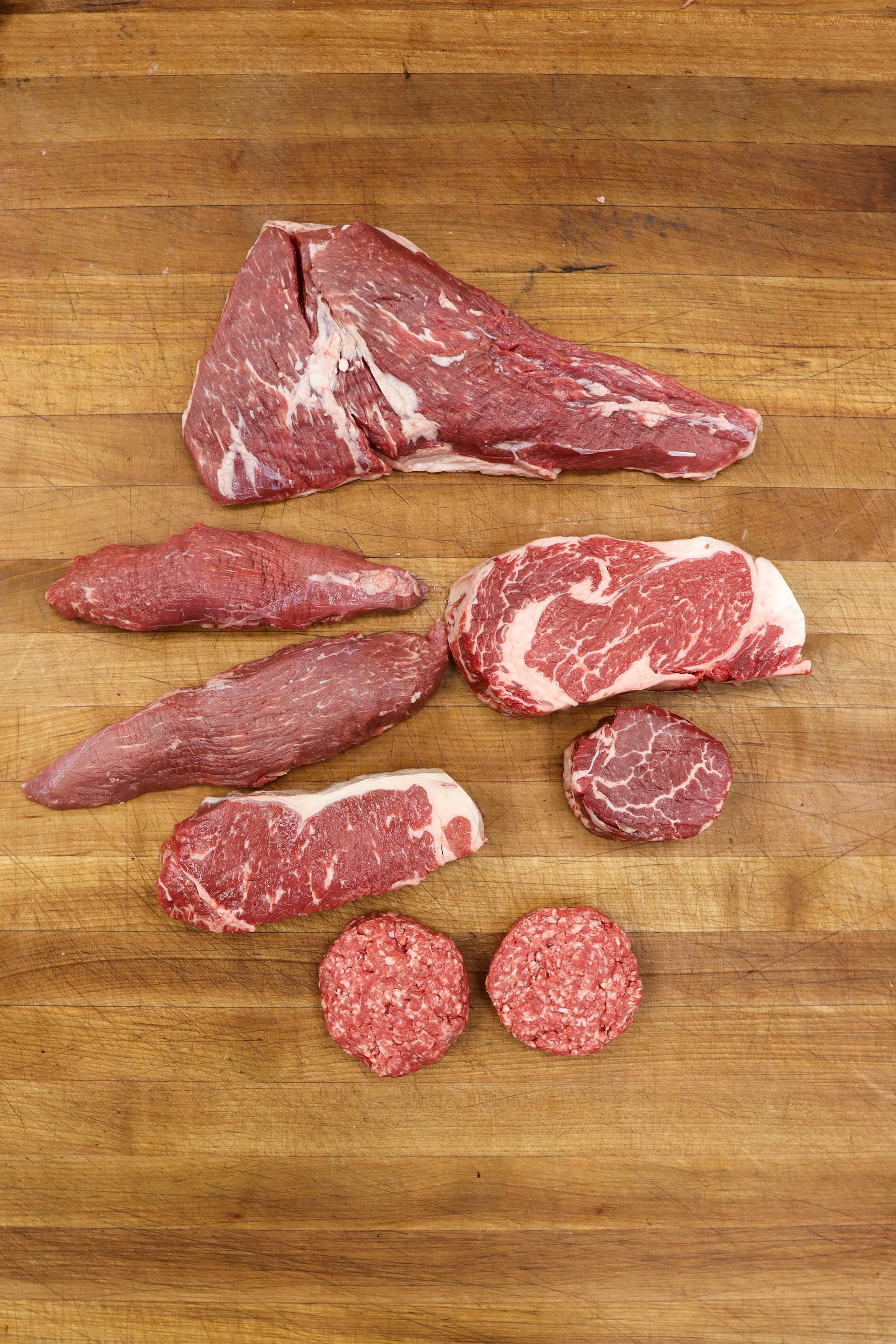 Assorted raw beef cuts arranged on a wooden cutting board.