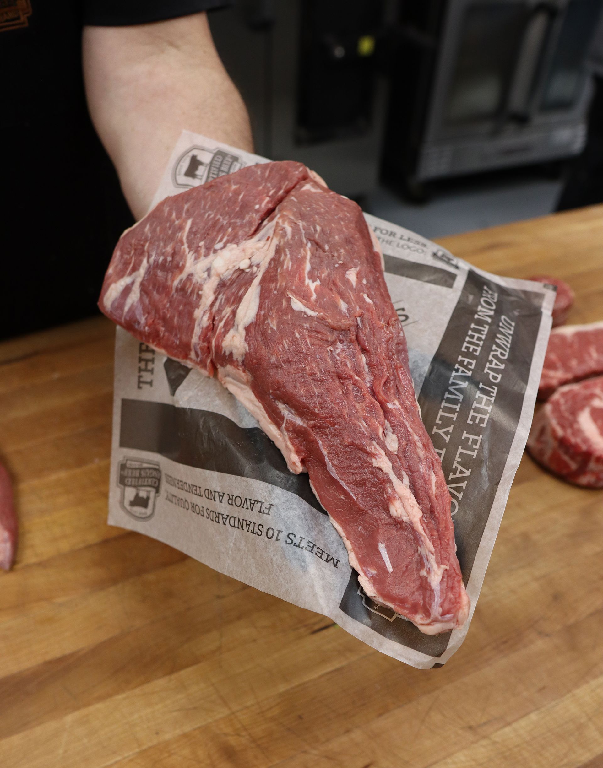Raw beef steak held in a hand over newspaper on a wooden cutting board