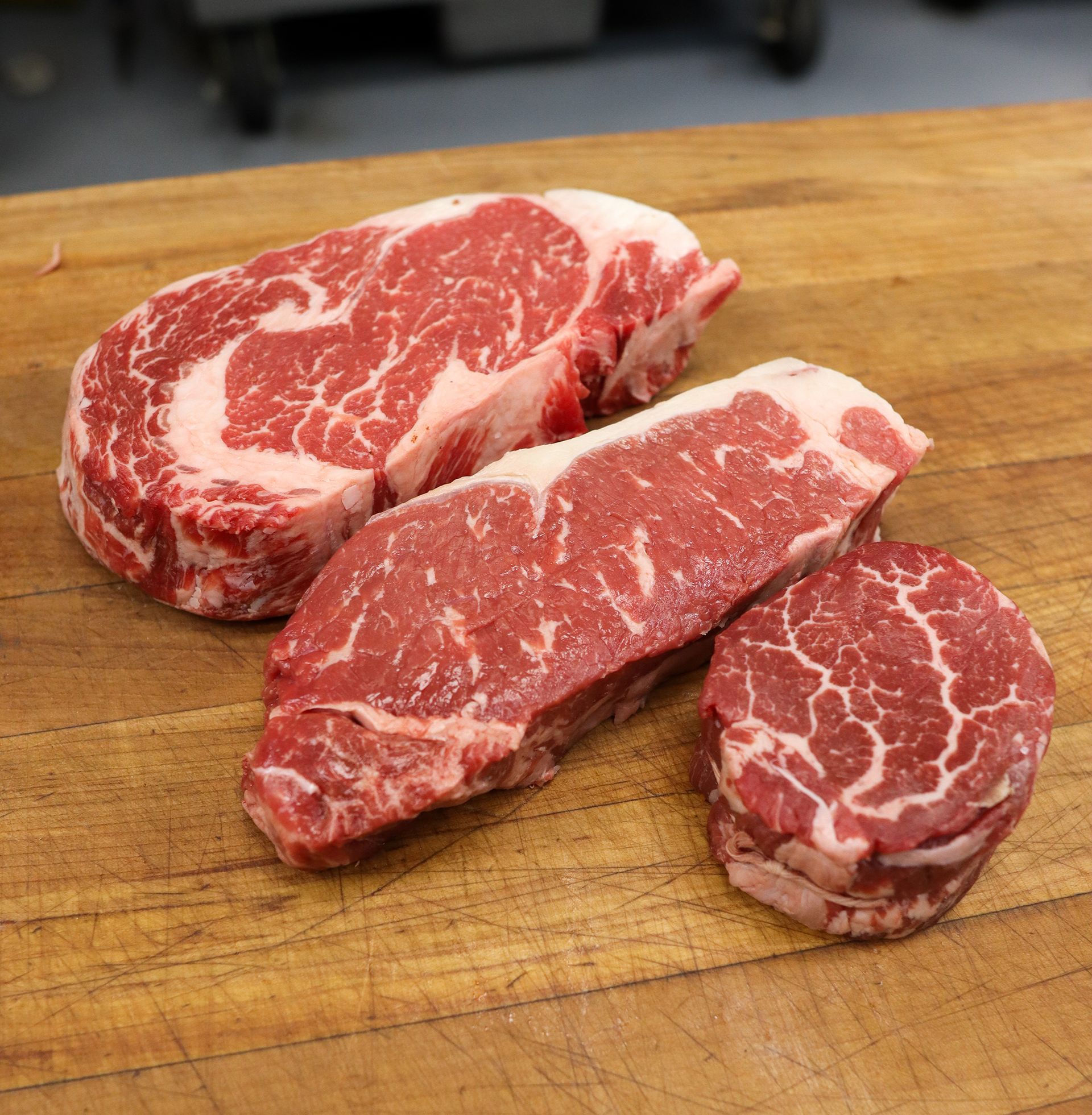Three raw marbled beef steaks on a wooden cutting board