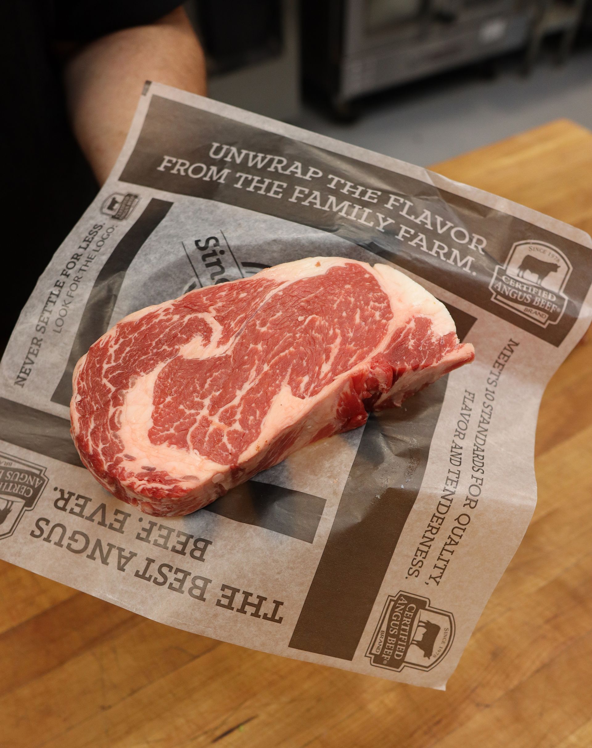 Raw marbled steak on branded butcher paper with “Unwrap the flavor” text.