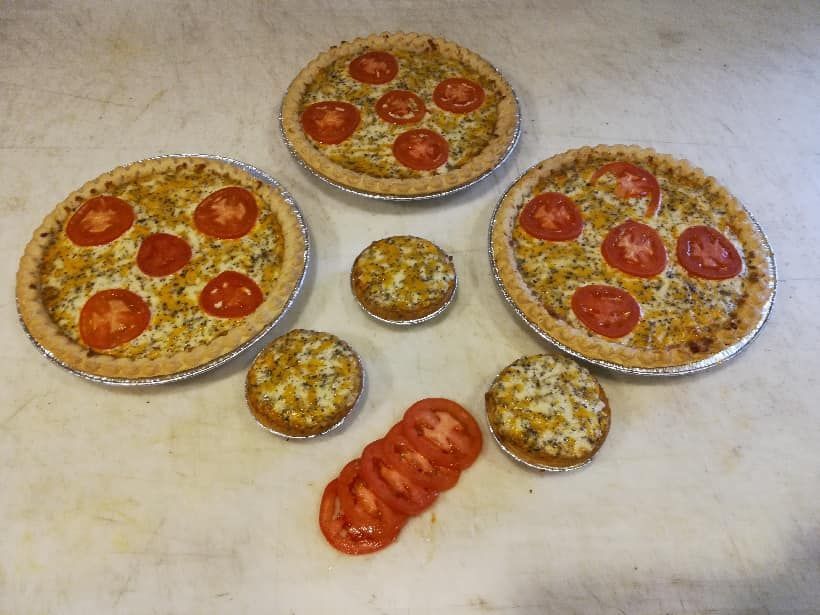 Various sizes of quiches with tomatoes on a white surface, with tomato slices.