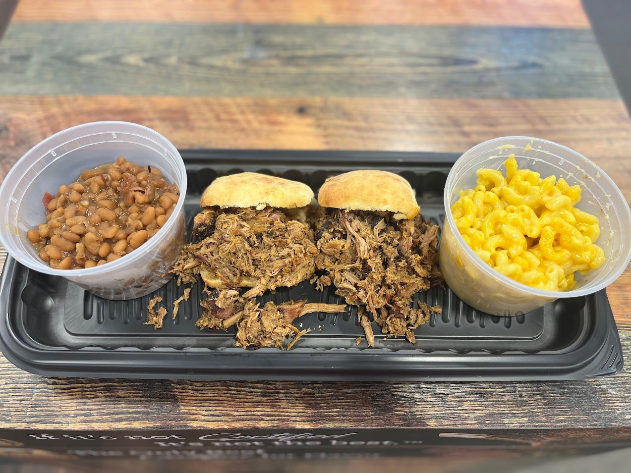 Pulled pork sandwiches with baked beans and mac and cheese in containers on a tray.
