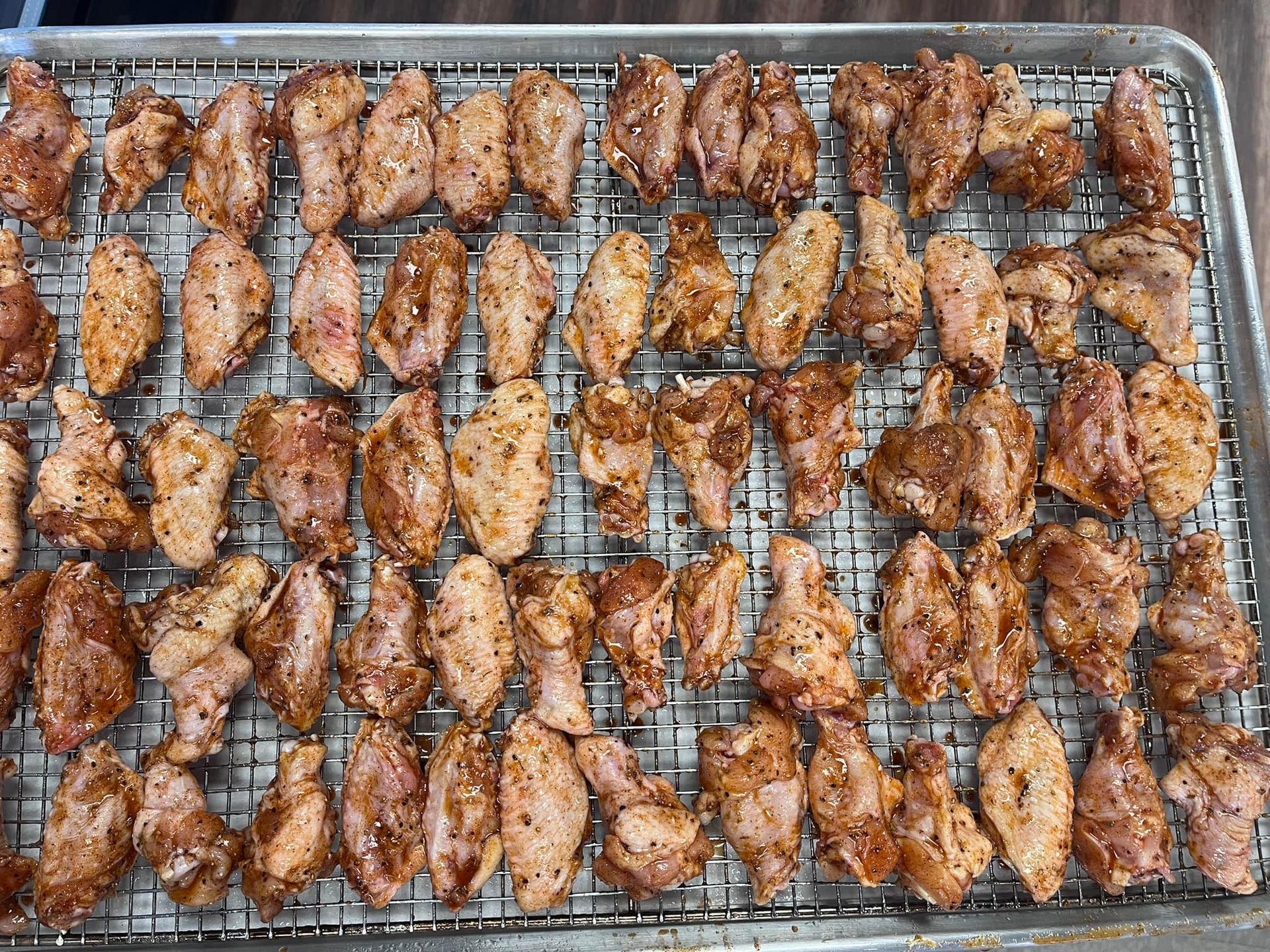 Raw seasoned chicken wings on a metal rack ready for cooking.