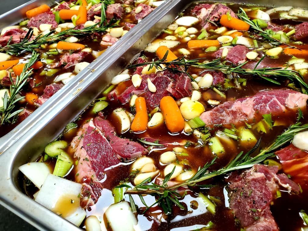 Raw beef with vegetables, herbs, and broth in a metal baking dish.