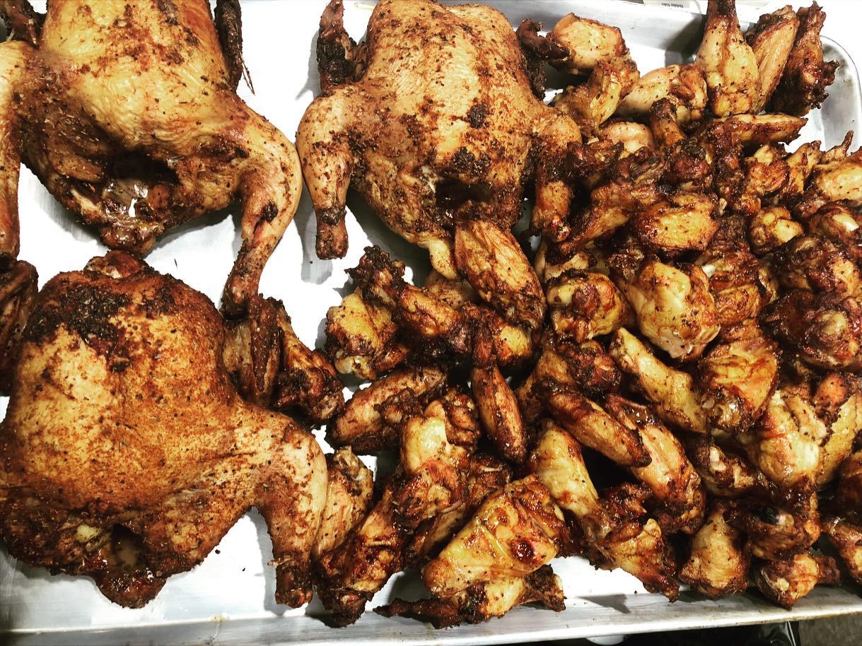 Roasted chickens and wings on a metal tray, seasoned with spices.