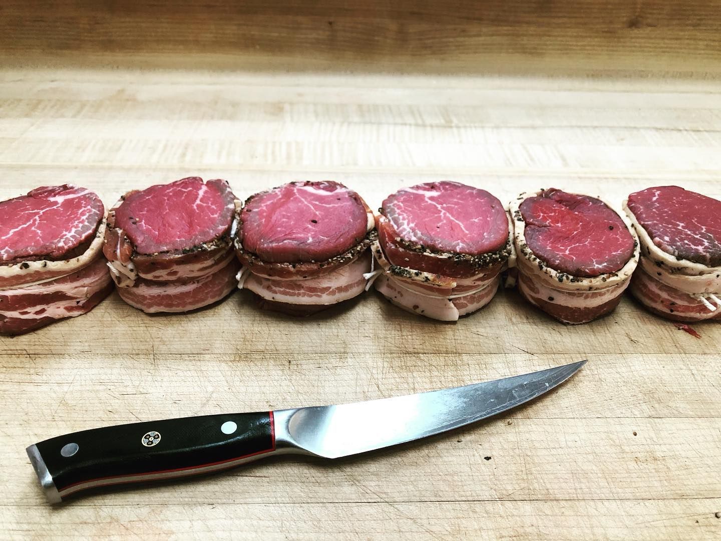 Six bacon-wrapped filet mignon steaks with a knife on a wooden surface.