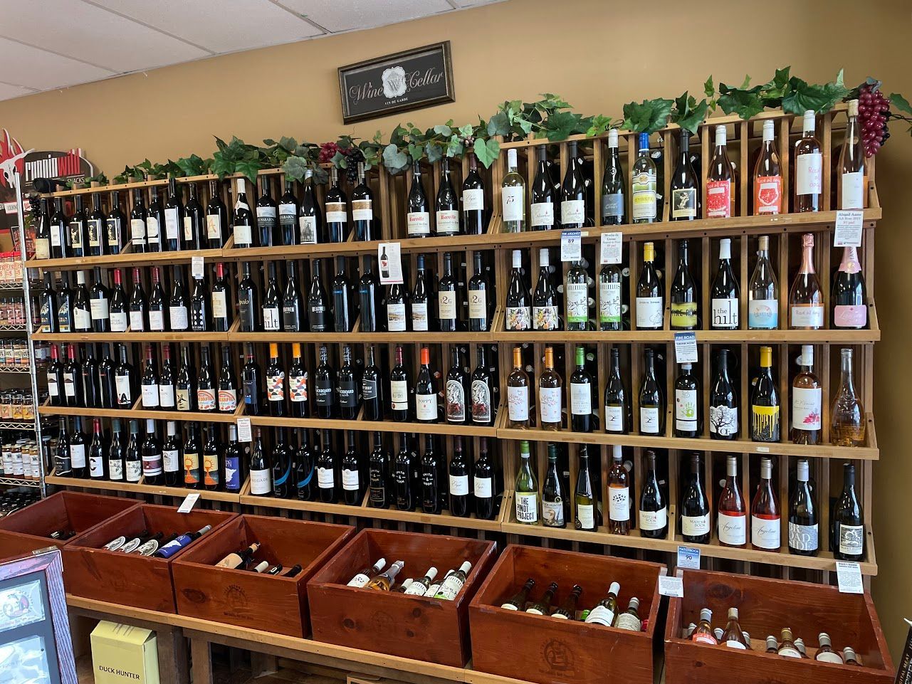 Wine bottles displayed on wooden shelves in a store, with crates in front filled with more bottles.