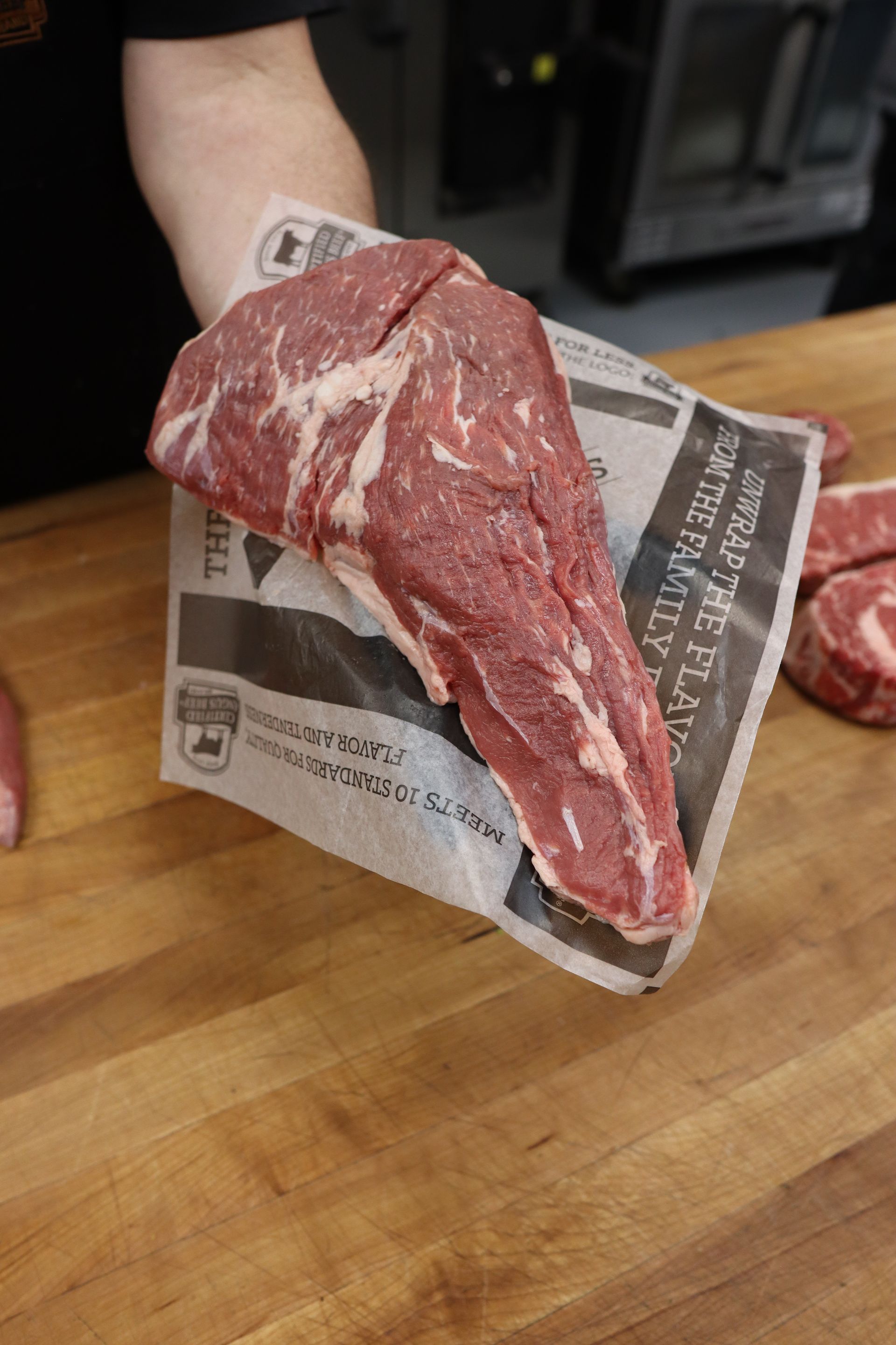 Raw beef cut on a newspaper-lined hand, over a wooden cutting board.