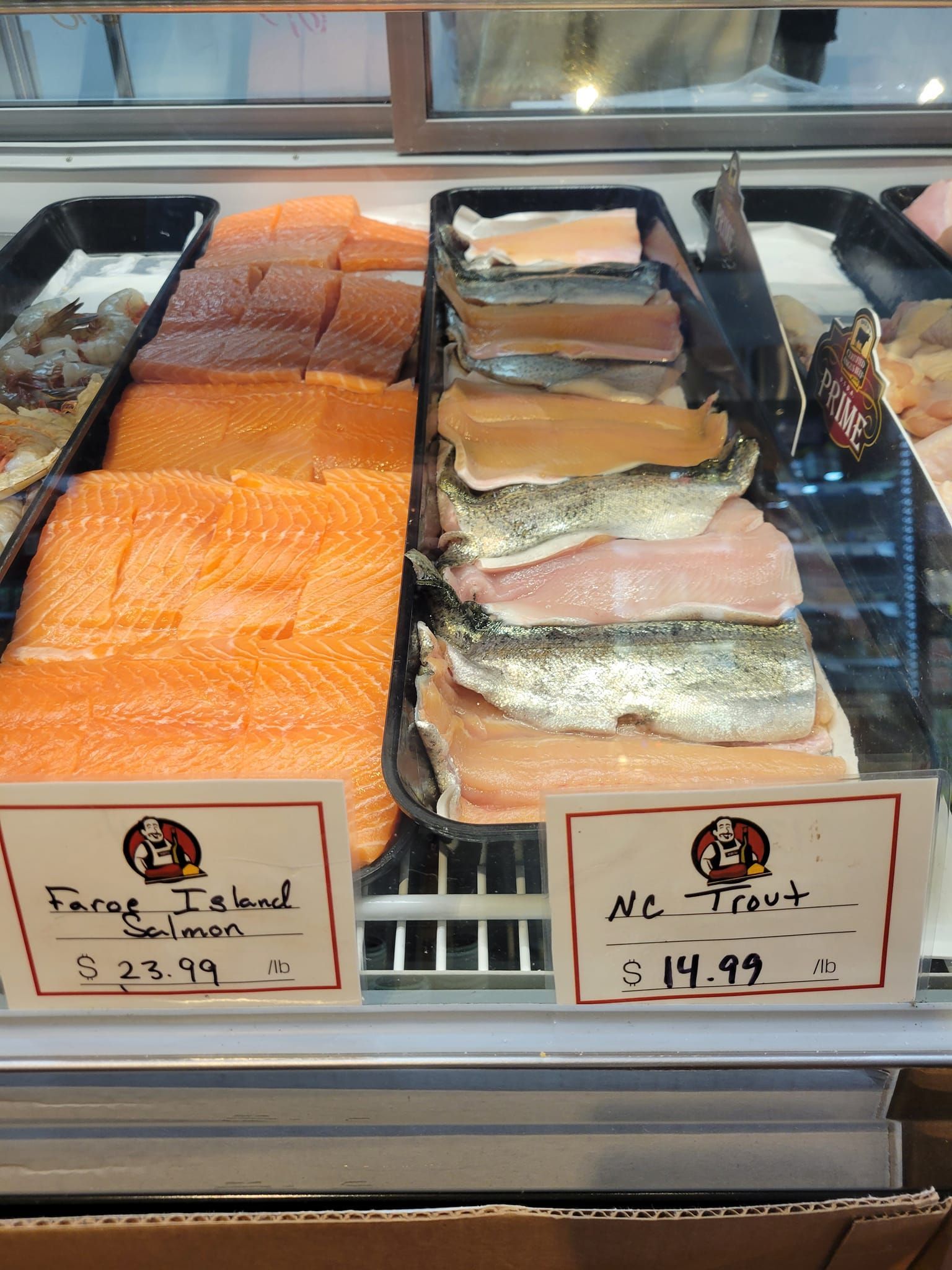 Fresh fish display case with salmon and trout, labeled with prices.