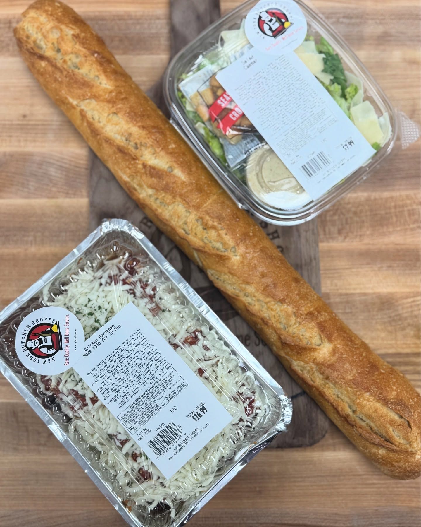 Baguette, Caesar salad, and a tray of lasagna on a wooden cutting board.