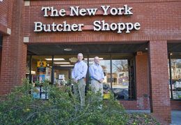 Man holding a large steak and a bottle of wine in a wine shop.