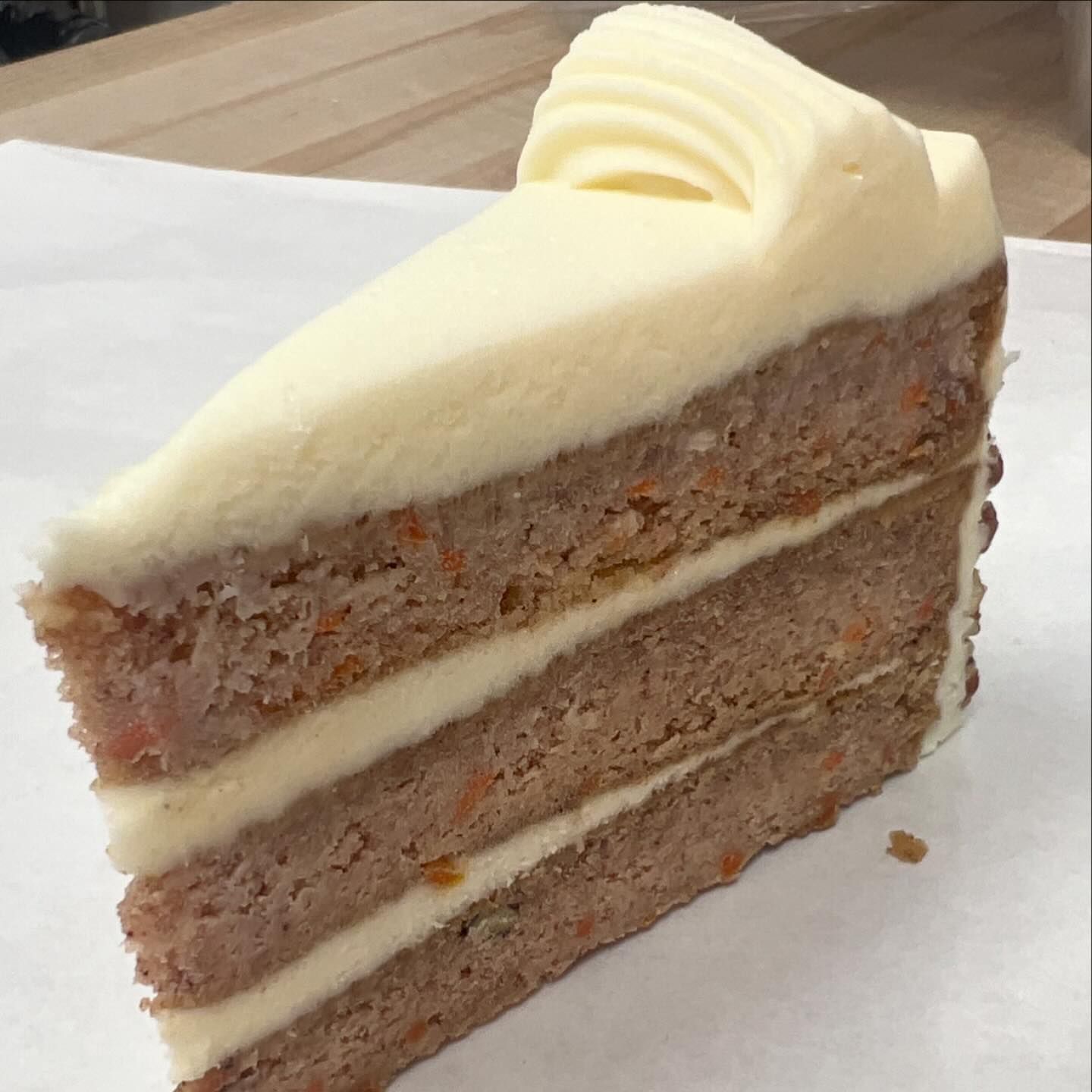 Slice of carrot cake with cream cheese frosting on white paper.