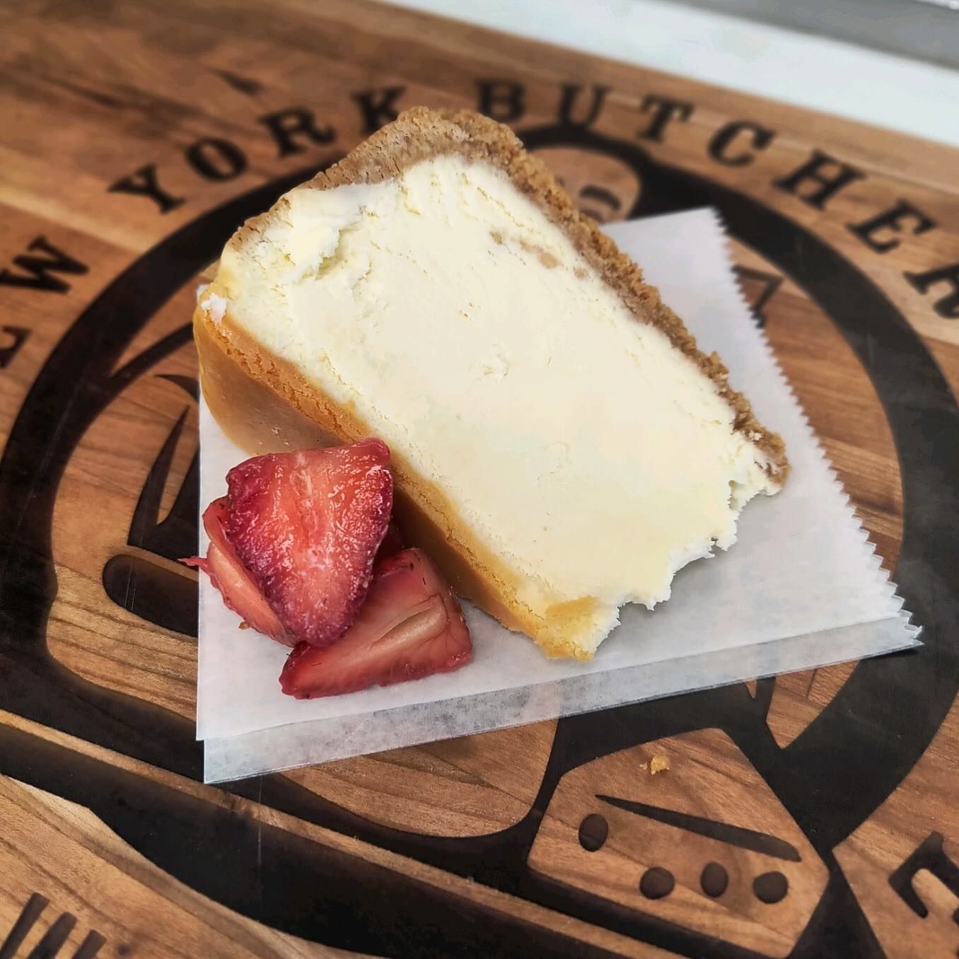 Slice of cheesecake with strawberries on a wooden butcher block.