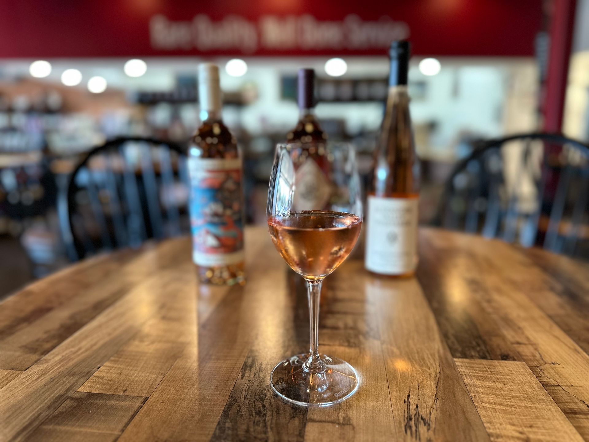 Wine glass with rosé on a wooden bar table, bottles blurred in the background