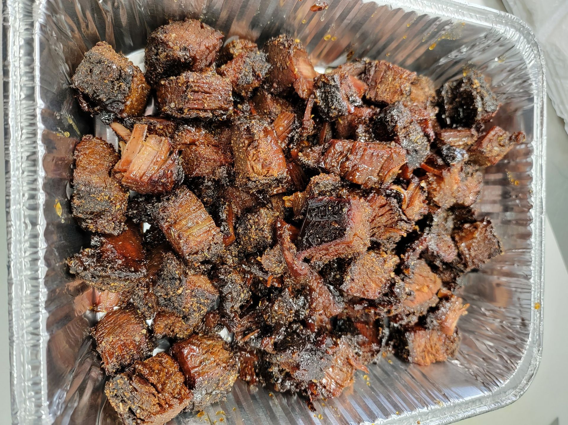Smoked, charred beef brisket burnt ends in a foil pan.
