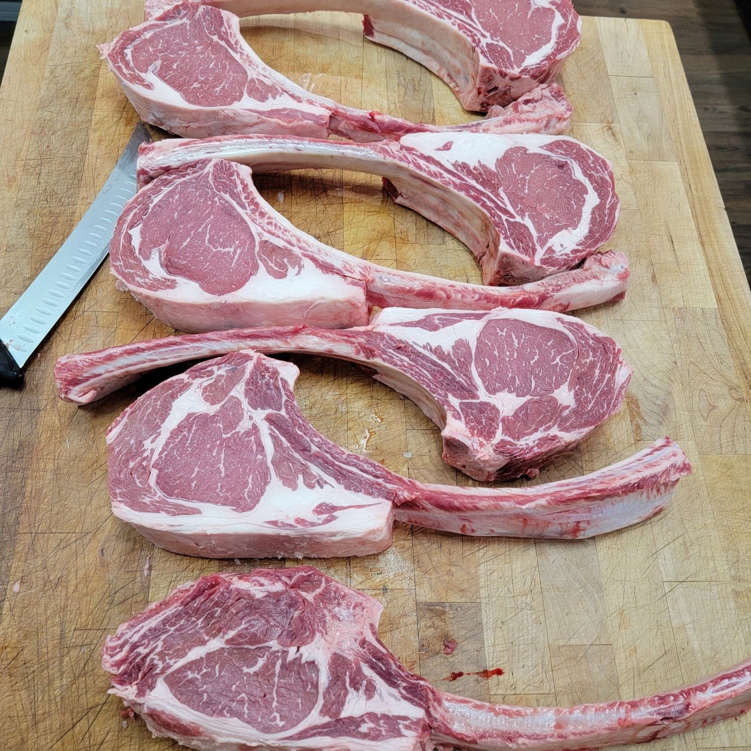 Three raw bone-in pork chops on a wooden cutting board with a knife