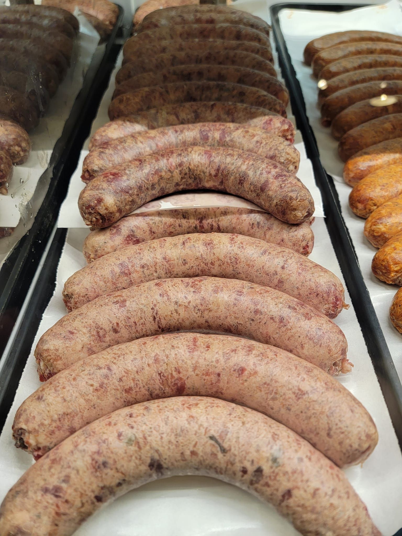 Display of various sausages in a butcher shop; brown, pink, and orange varieties on white paper.