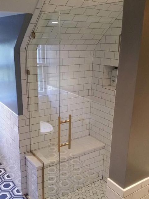 A bathroom with white tiles and a glass shower door.
