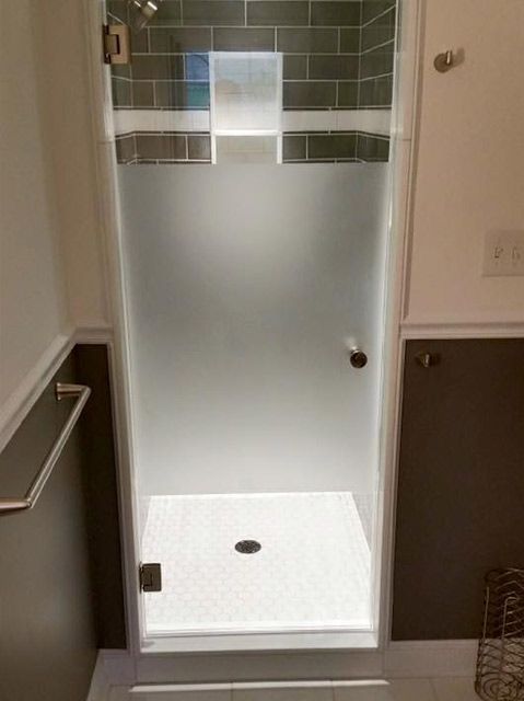 A bathroom with a walk in shower with a frosted glass door.