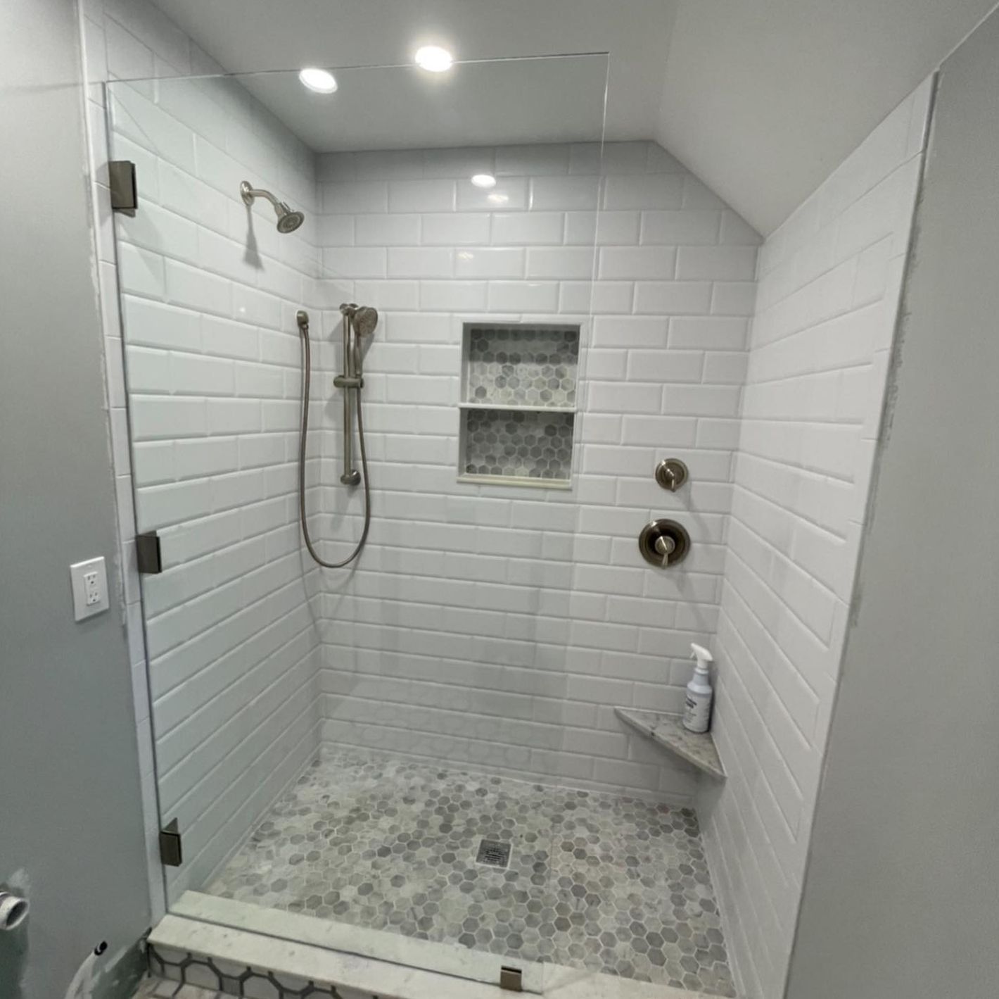A bathroom with white tiles and a walk in shower with a glass door.