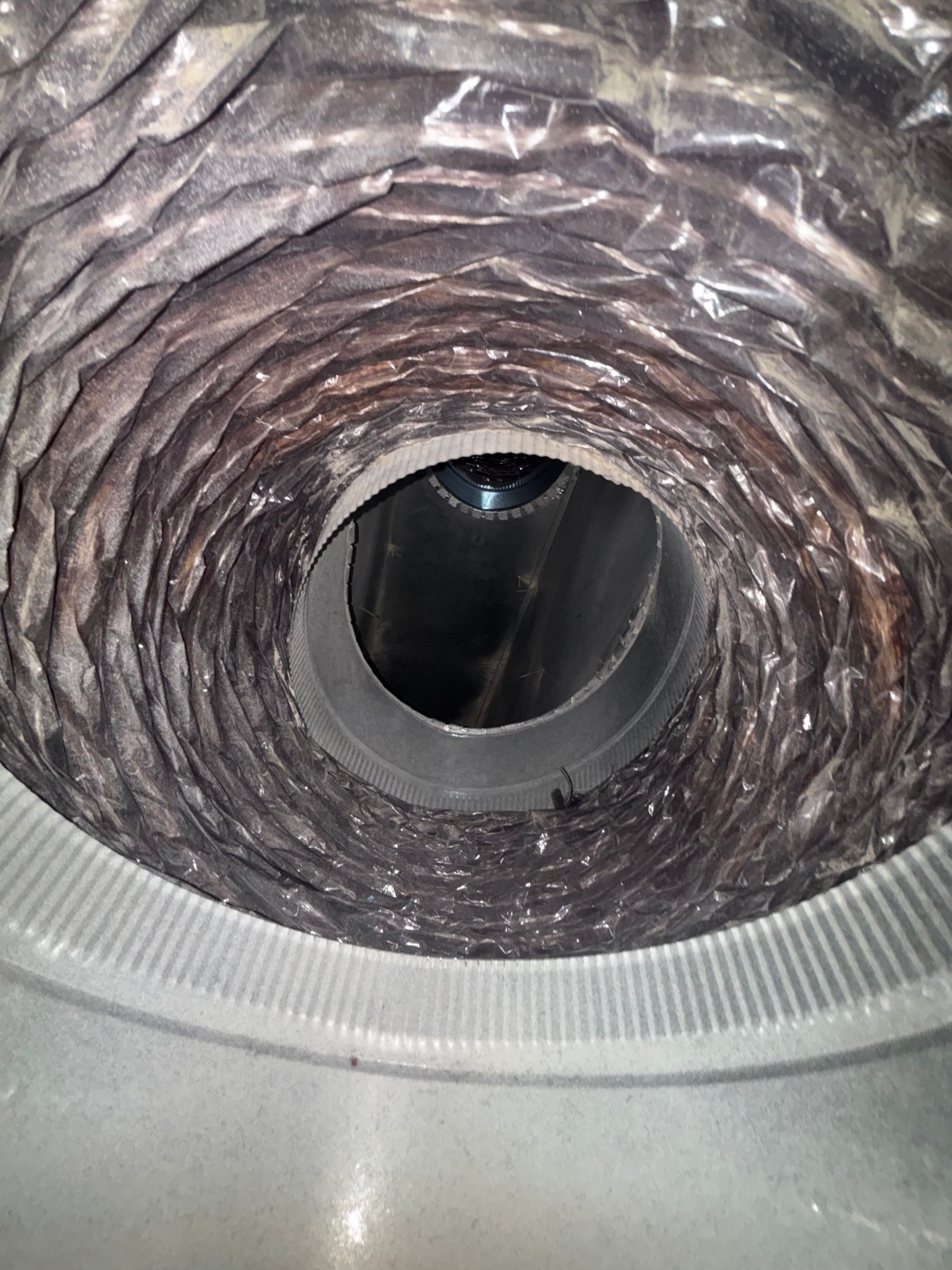 Close-up of a circular duct lined with wrinkled insulation and a dark opening in the center.