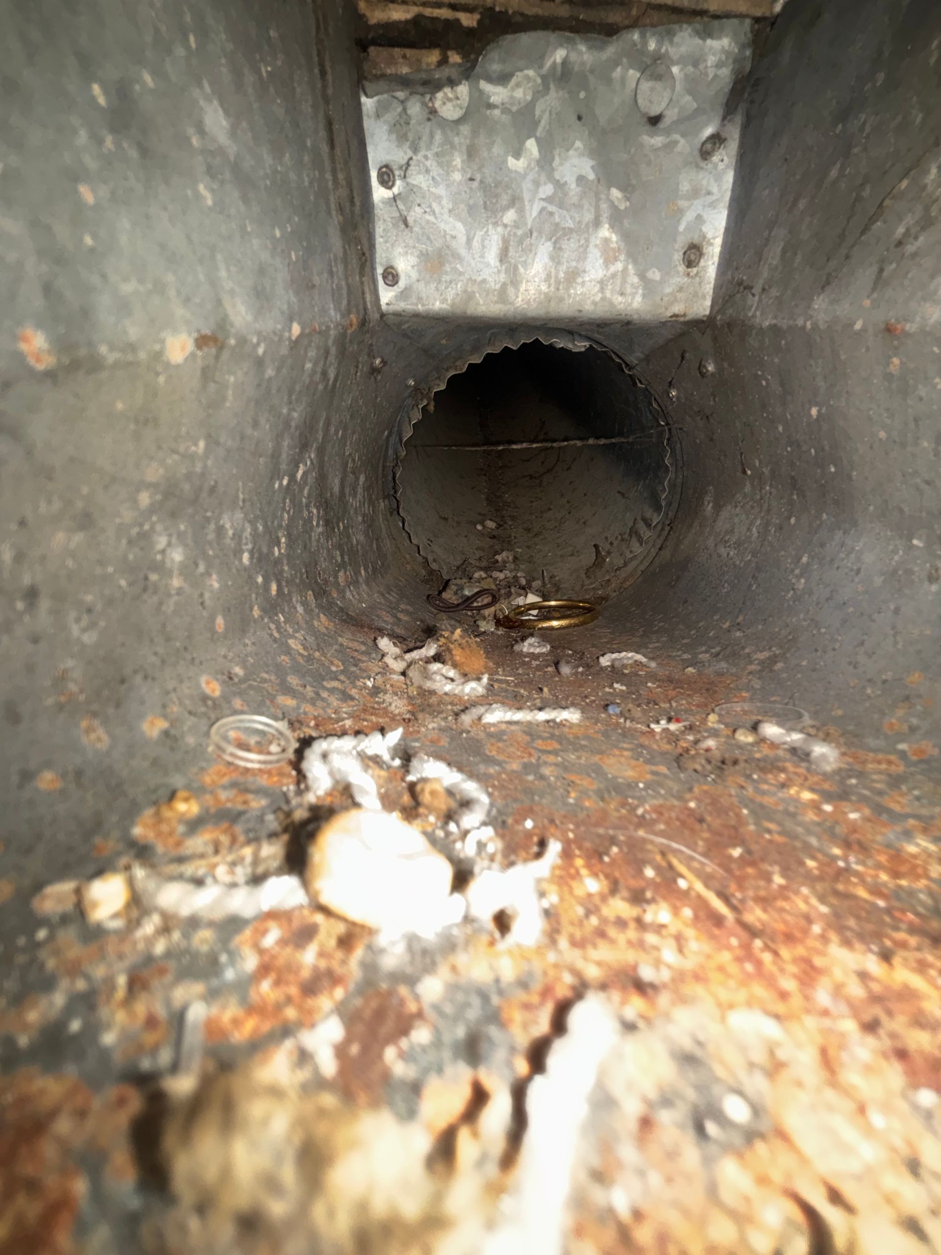 Rusty metal pipe interior with debris and corrosion buildup inside a dark duct