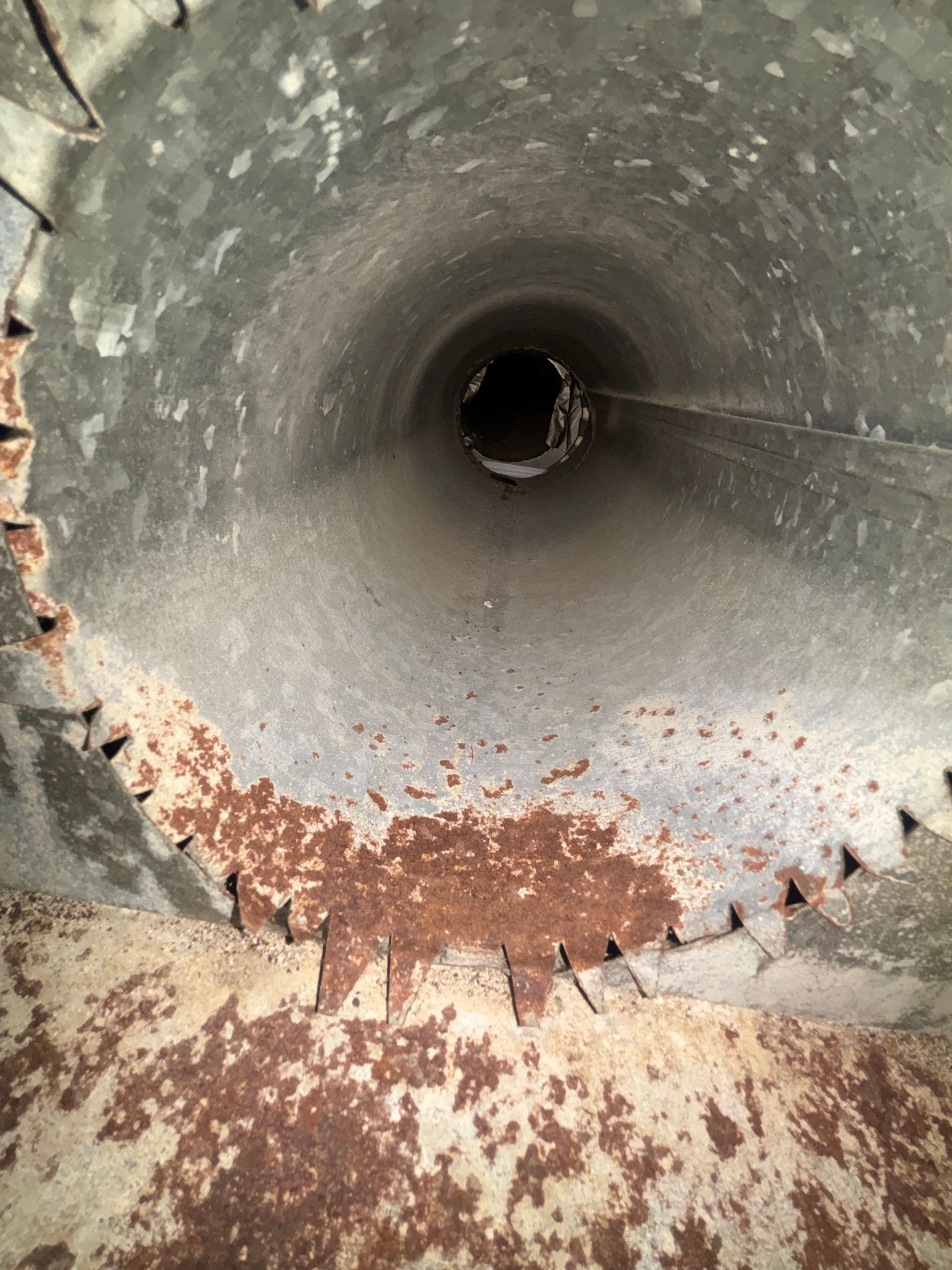 Rusty metal pipe interior with corroded edges and a dark circular opening in the center