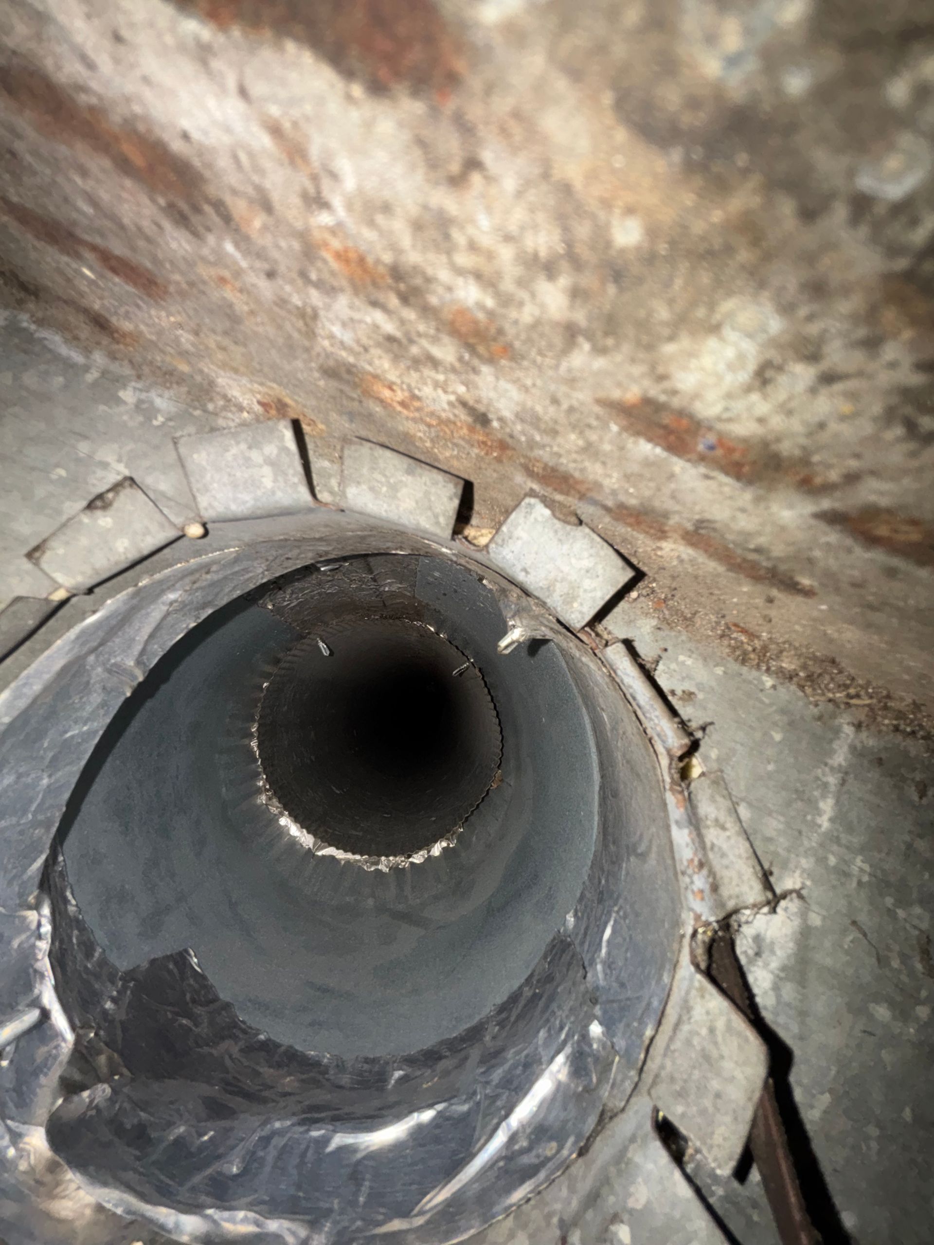 Close-up of a damaged metal pipe inside a cracked concrete wall opening