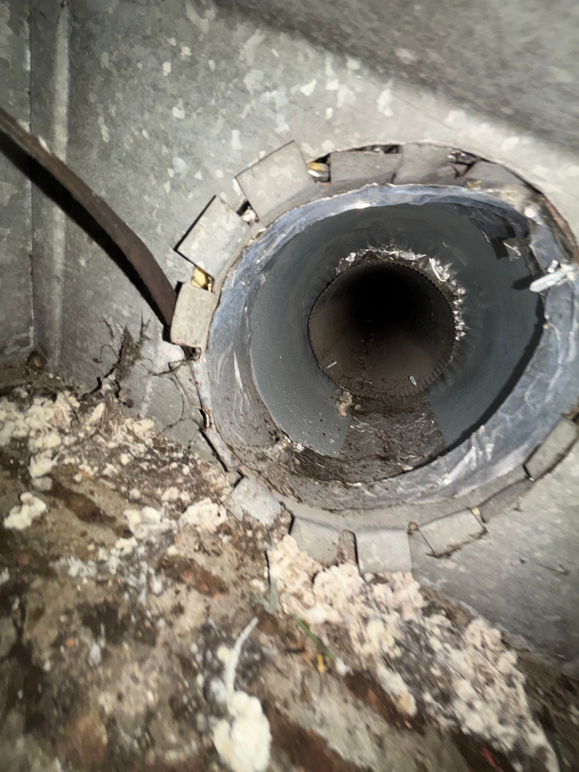 Close-up of a damaged circular pipe opening in a concrete wall, surrounded by debris and grime