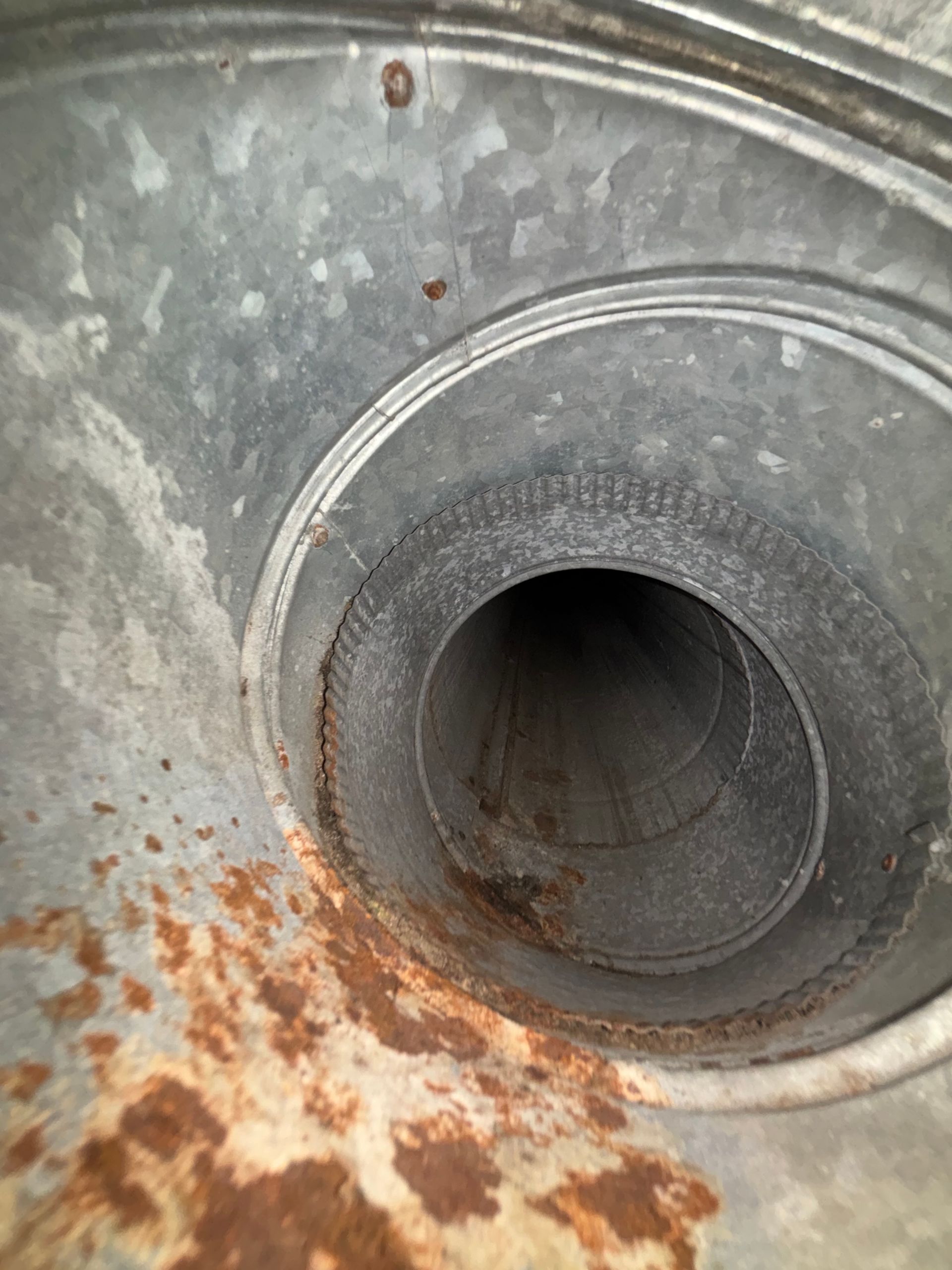 Close-up of a rusted metal pipe opening with corrosion and gray, weathered surface.