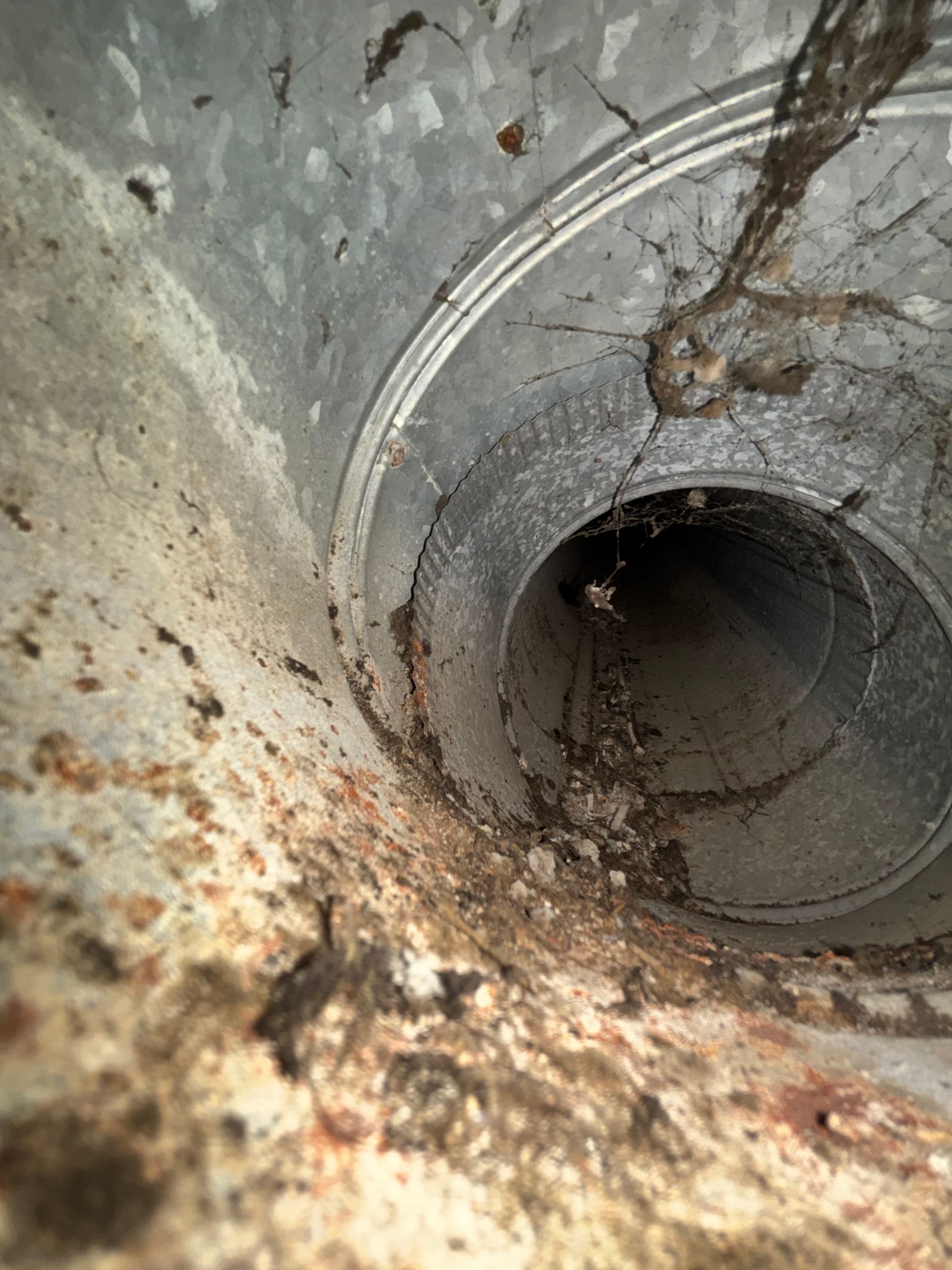 Rusty concrete drain pipe opening with debris and grime inside