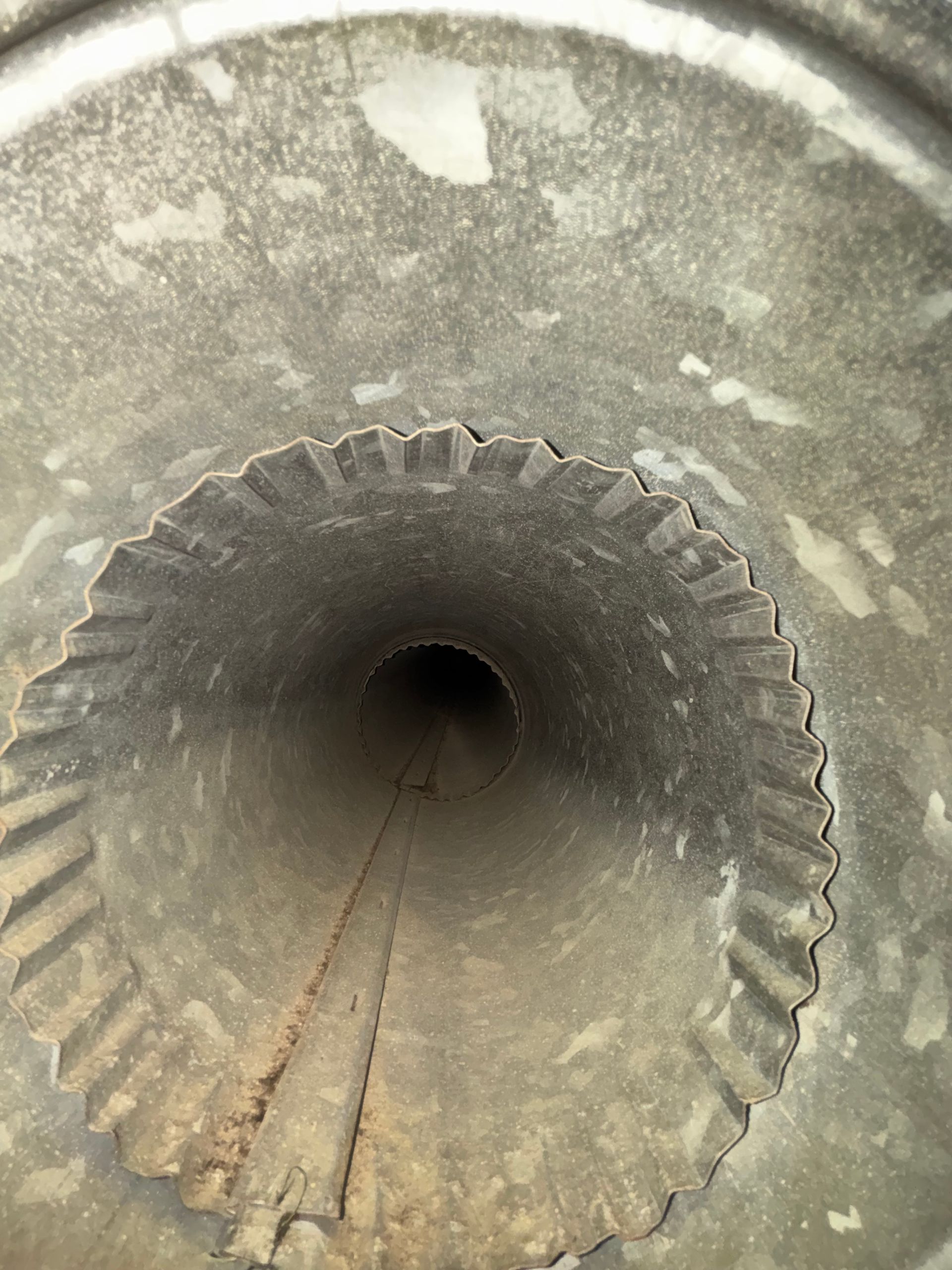 Inside view of a corrugated metal pipe with a dark circular opening and dirt at the bottom
