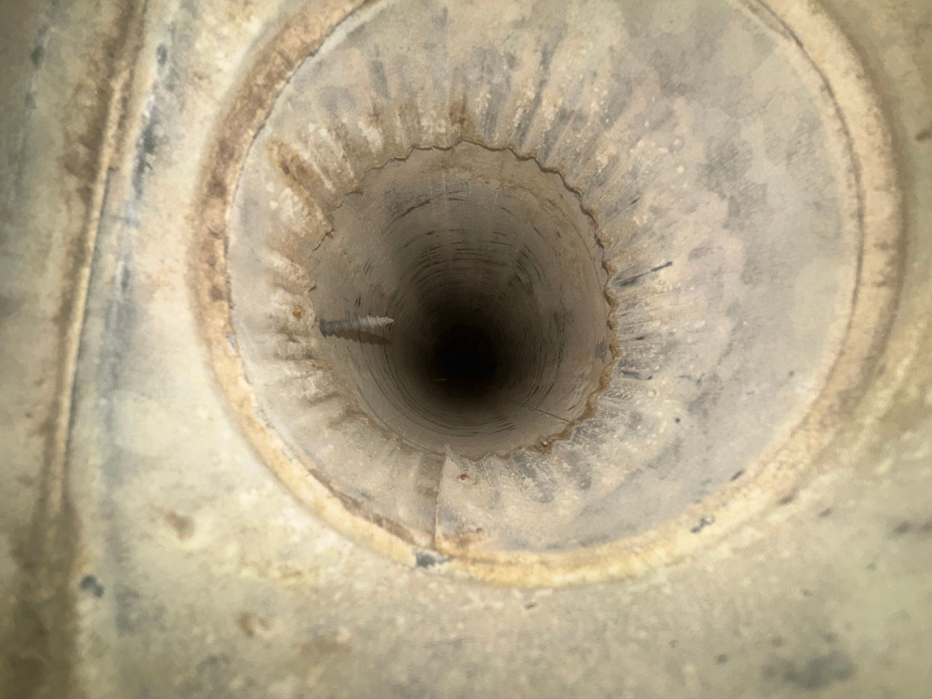 Close-up of a dusty circular pipe opening with a dark center and beige, worn edges