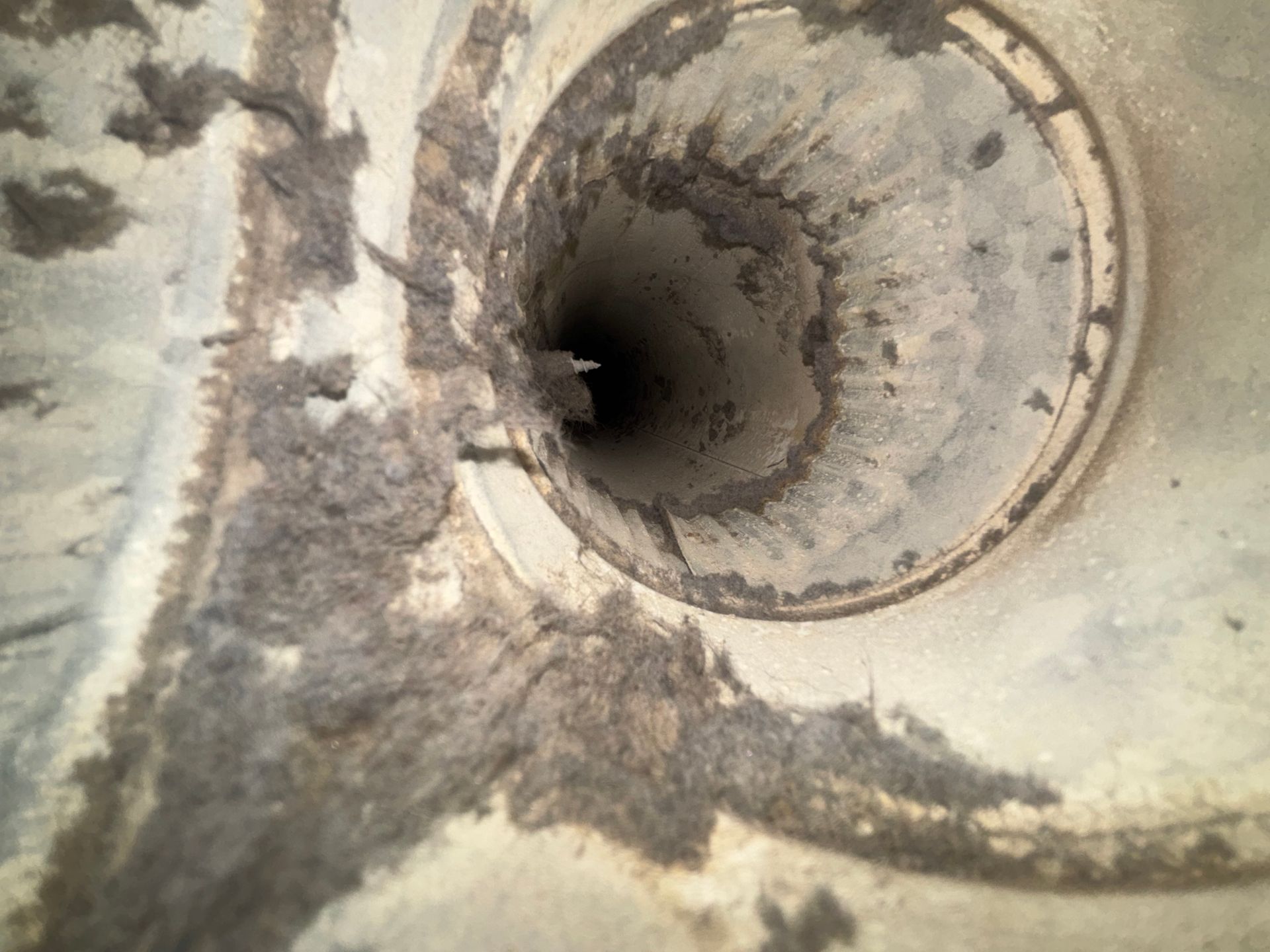 Close-up of a concrete drain opening with dark water and a stained, rough surface.